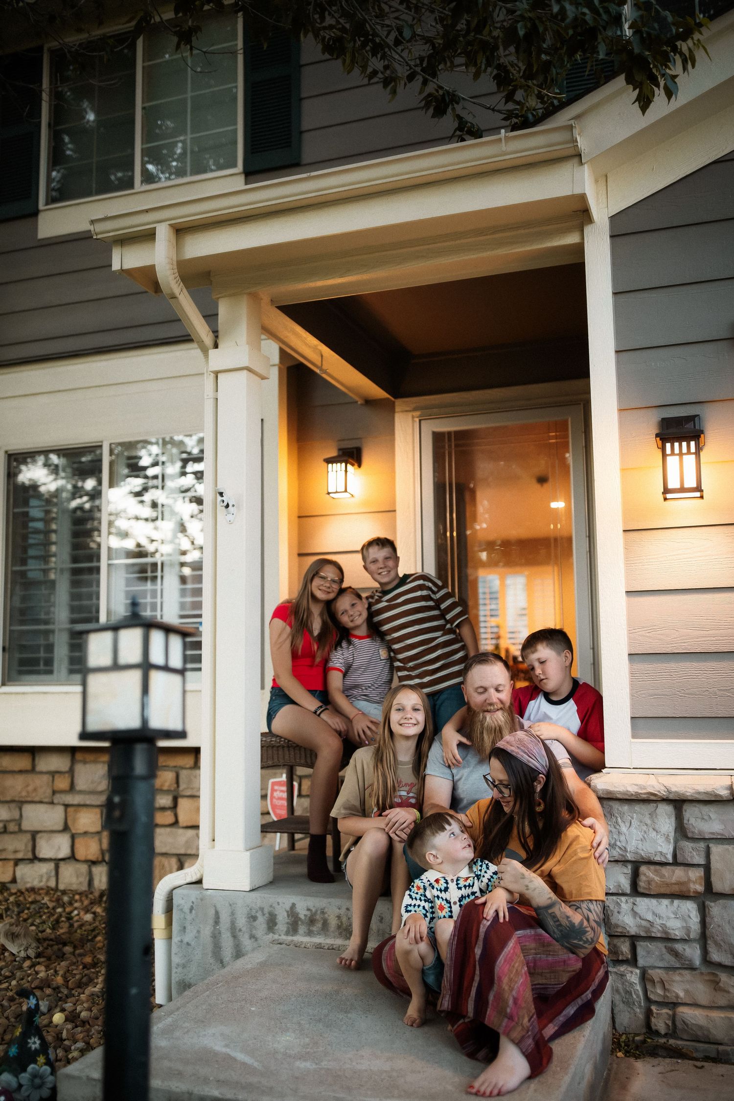 Large family posing together on front porch steps of a cozy home at dusk, smiling warmly.