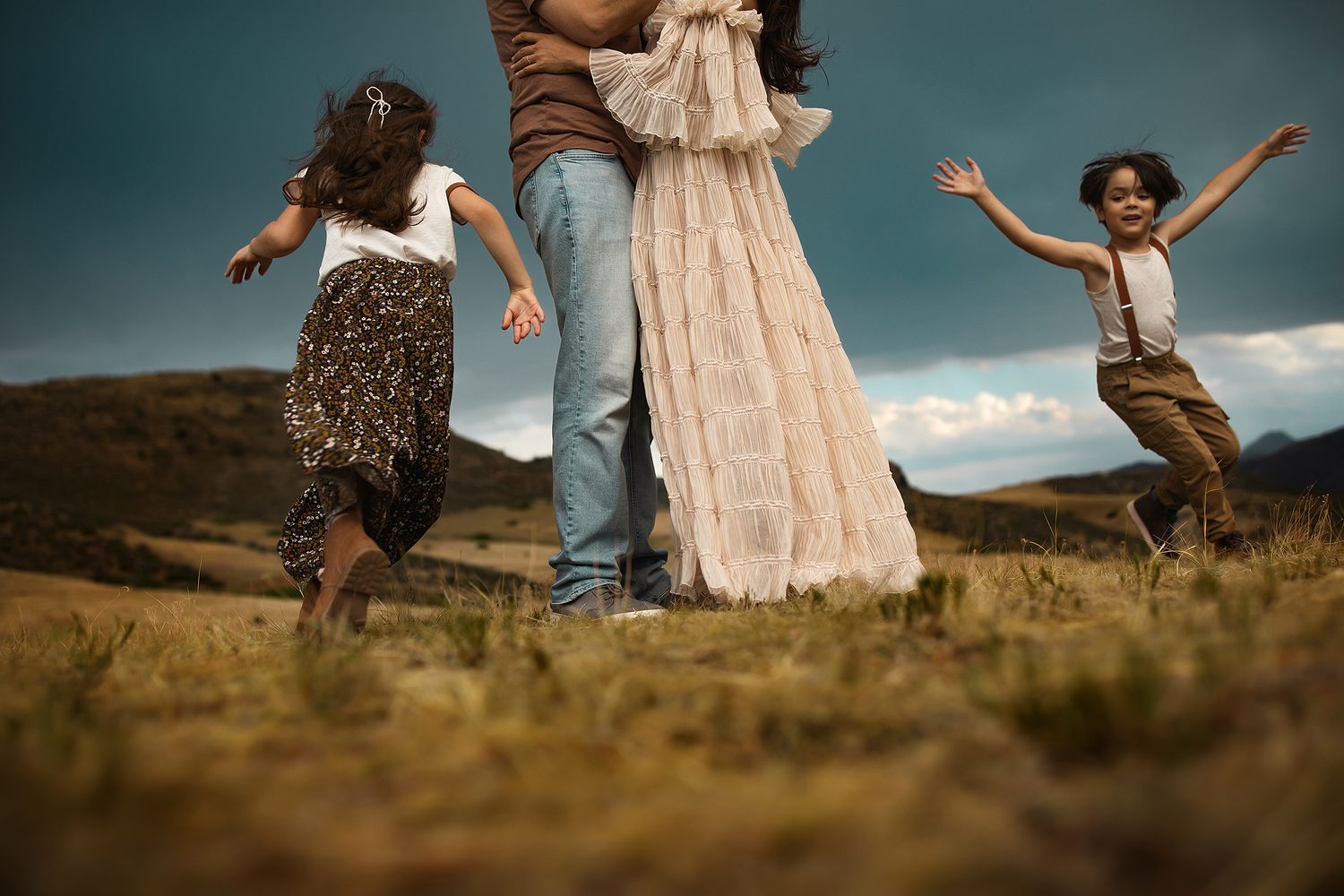 A couple in casual and formal attire playfully dances and poses together in a scenic field during golden hour.