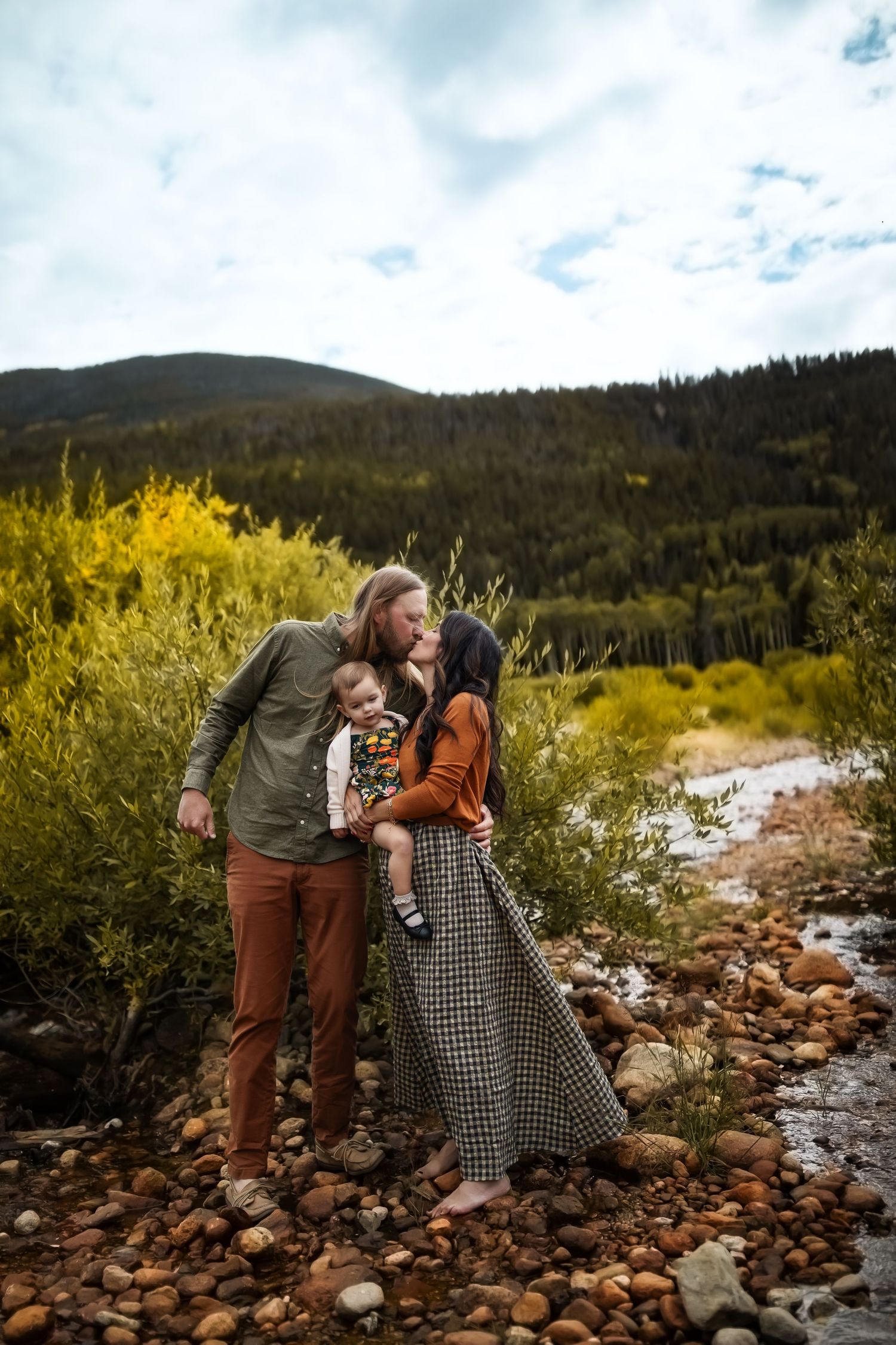 Candid moment captured by rocky riverside with mountains and fall foliage in background.