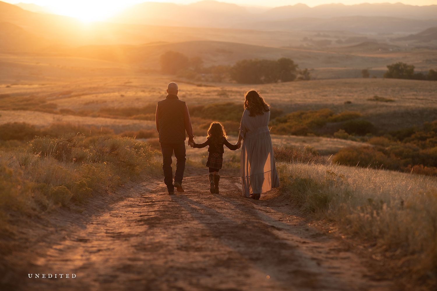 Silhouettes walking along a dirt path during golden hour in rolling hills.