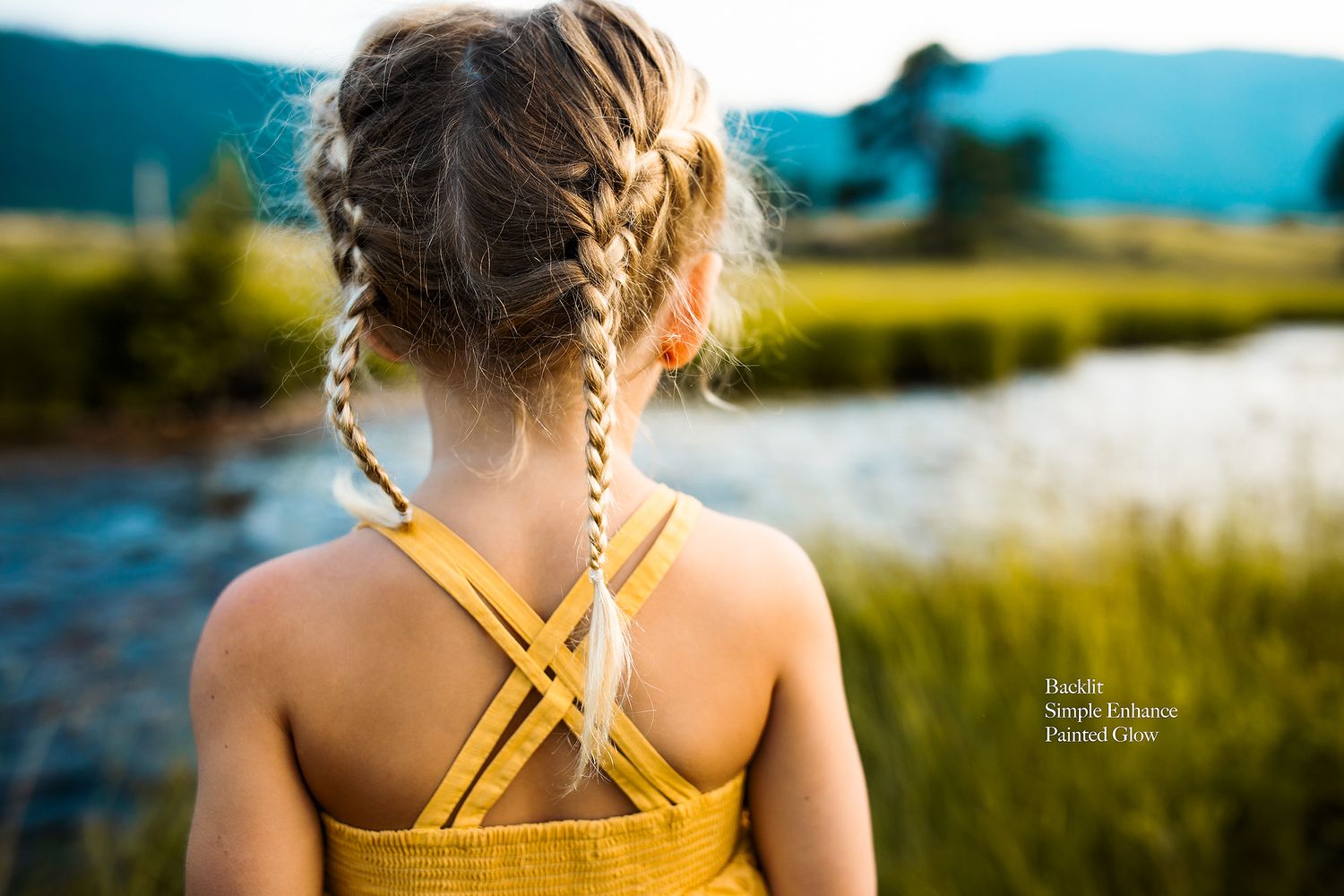Young person with braided hair wearing a yellow top looks out over a serene lake.