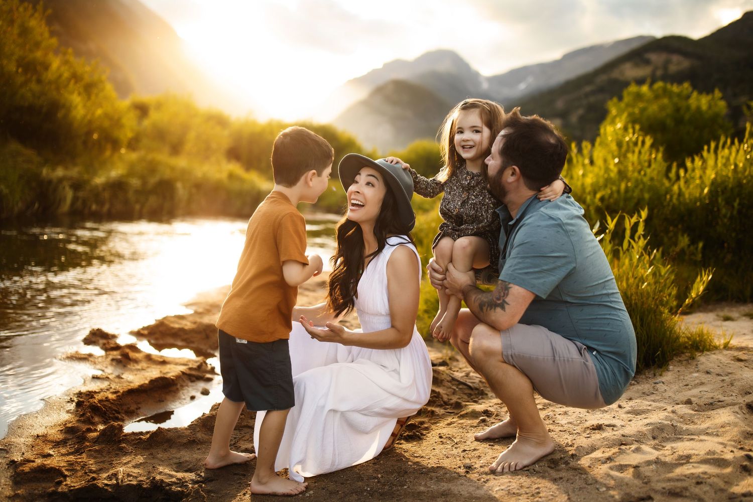 Family enjoying a sunset picnic together on a rocky beach with golden light filtering through the clouds.