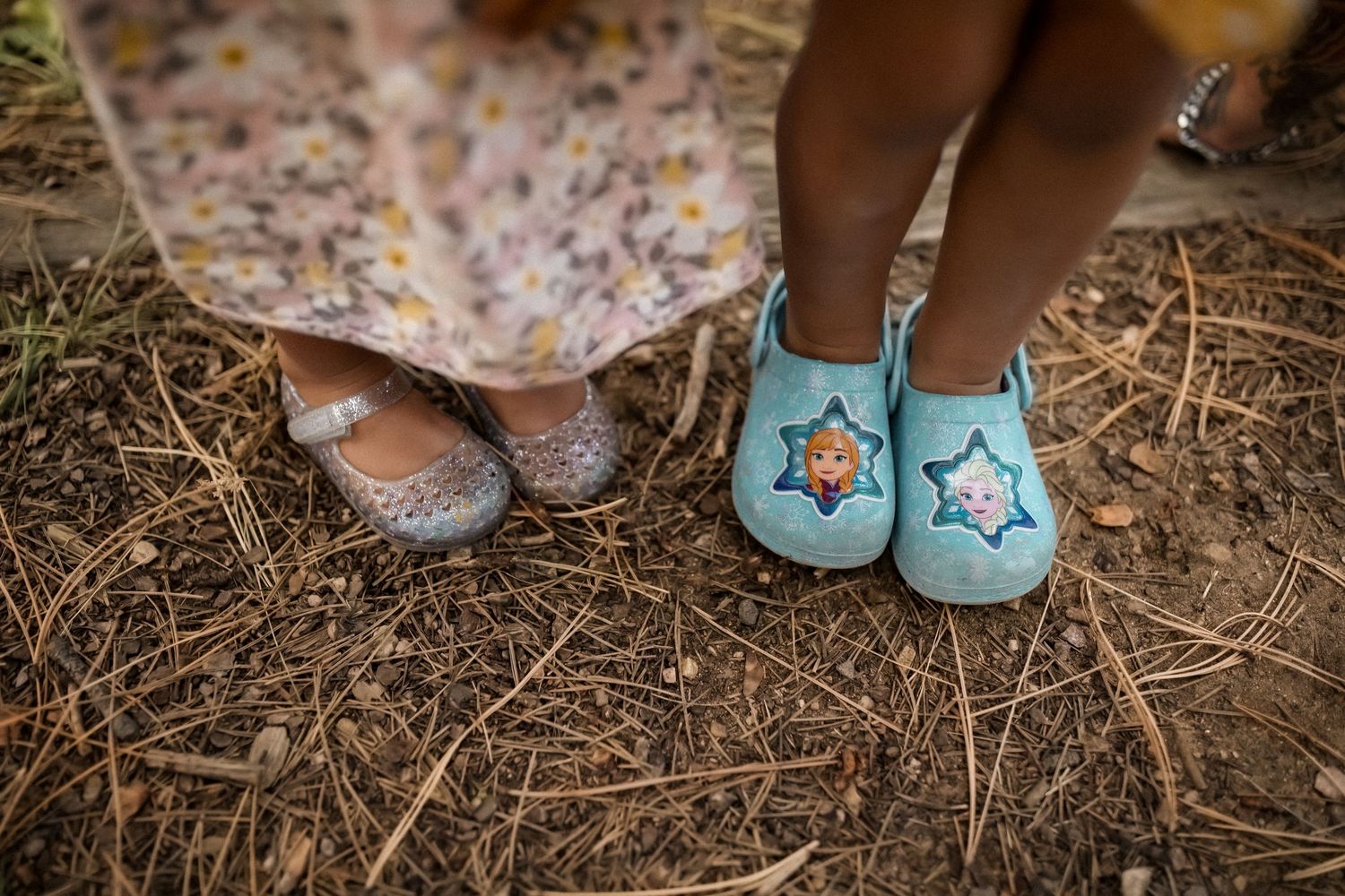 Two pairs of feet wearing contrasting shoes - one in sparkly flats and one in light blue slippers with star designs.