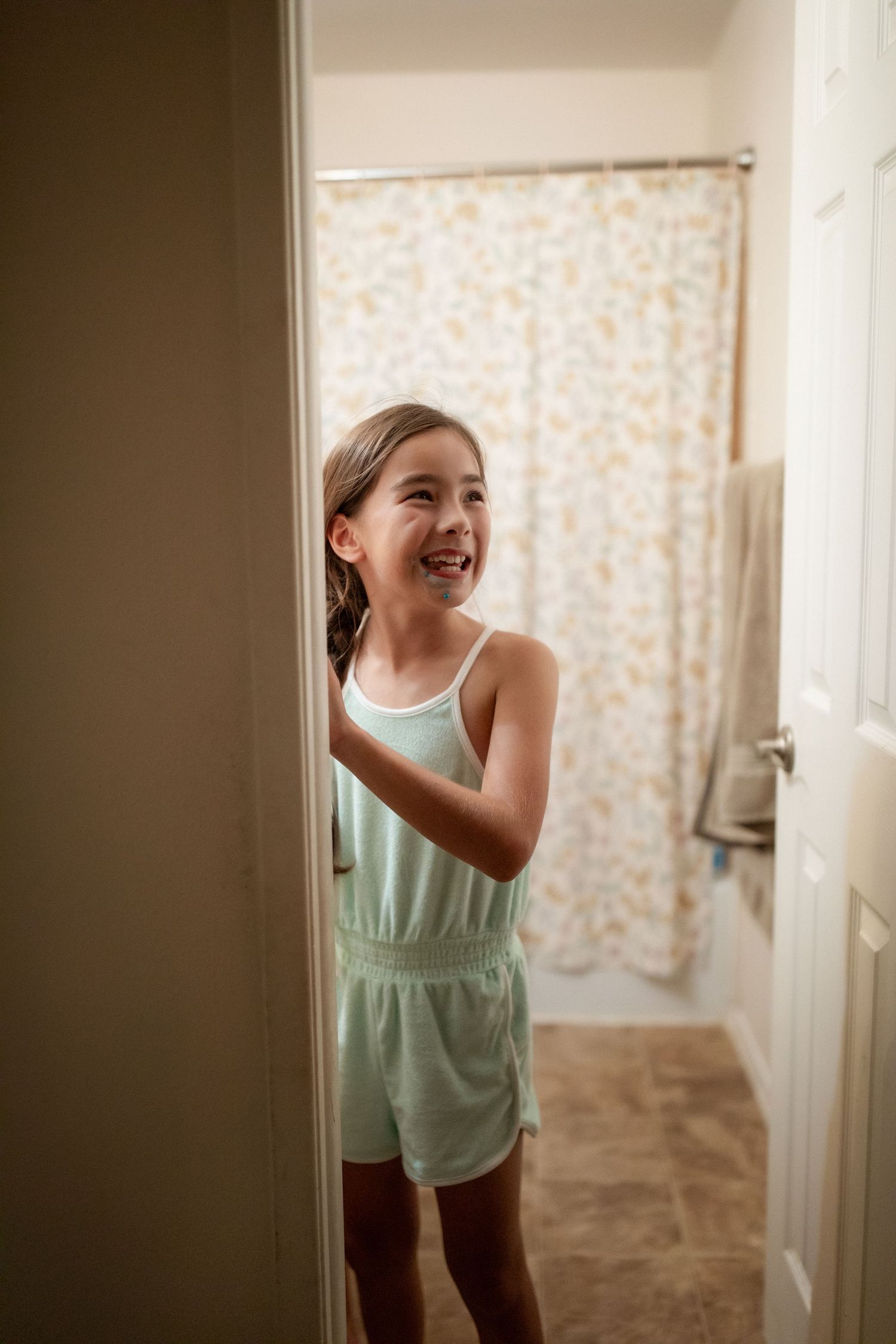 A child in a mint green top playfully peeks around a doorway in a sequence of candid shots.