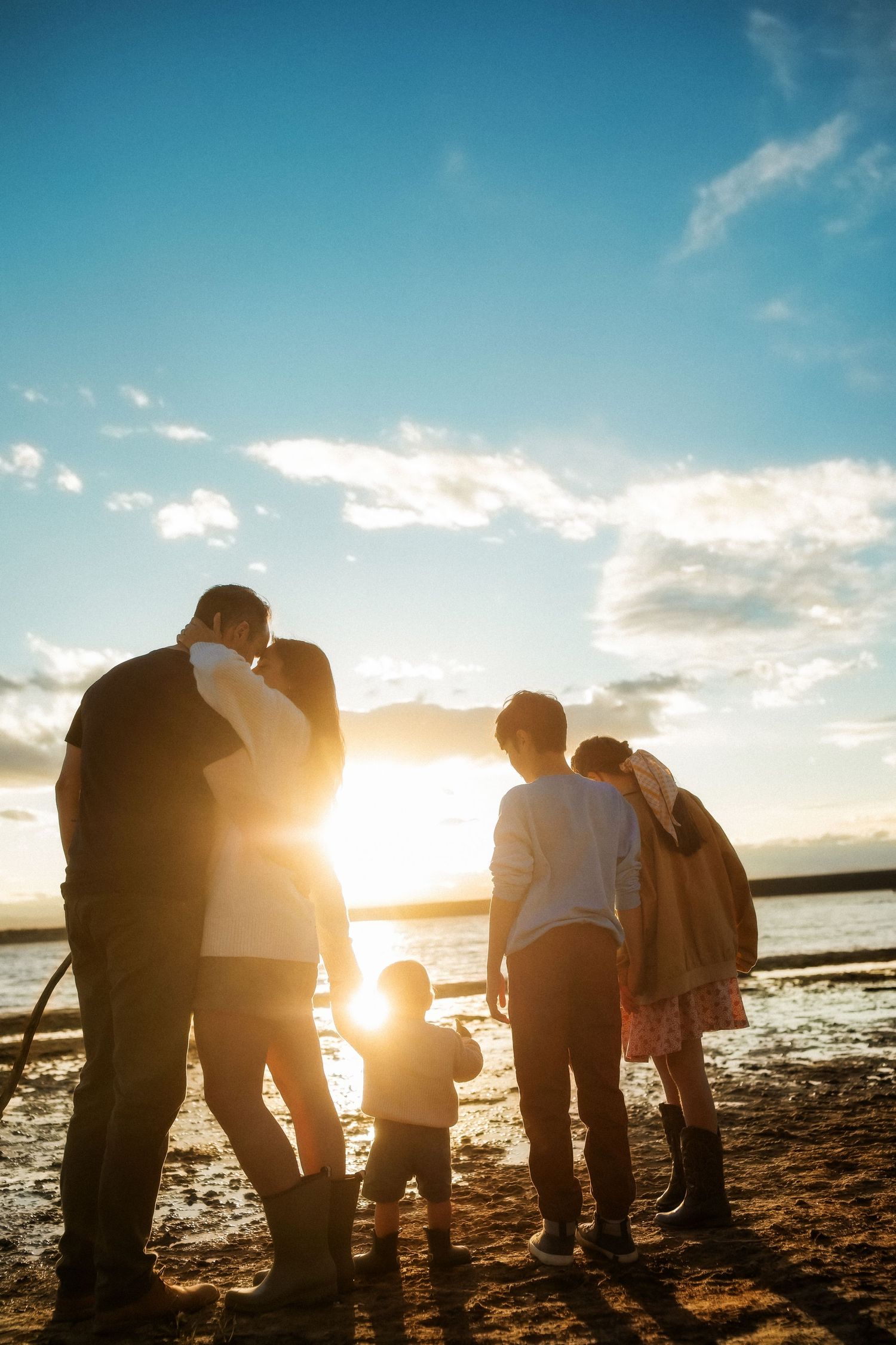 Family silhouetted against a golden sunset on a beach, with adults and children sharing a tender moment by the water.