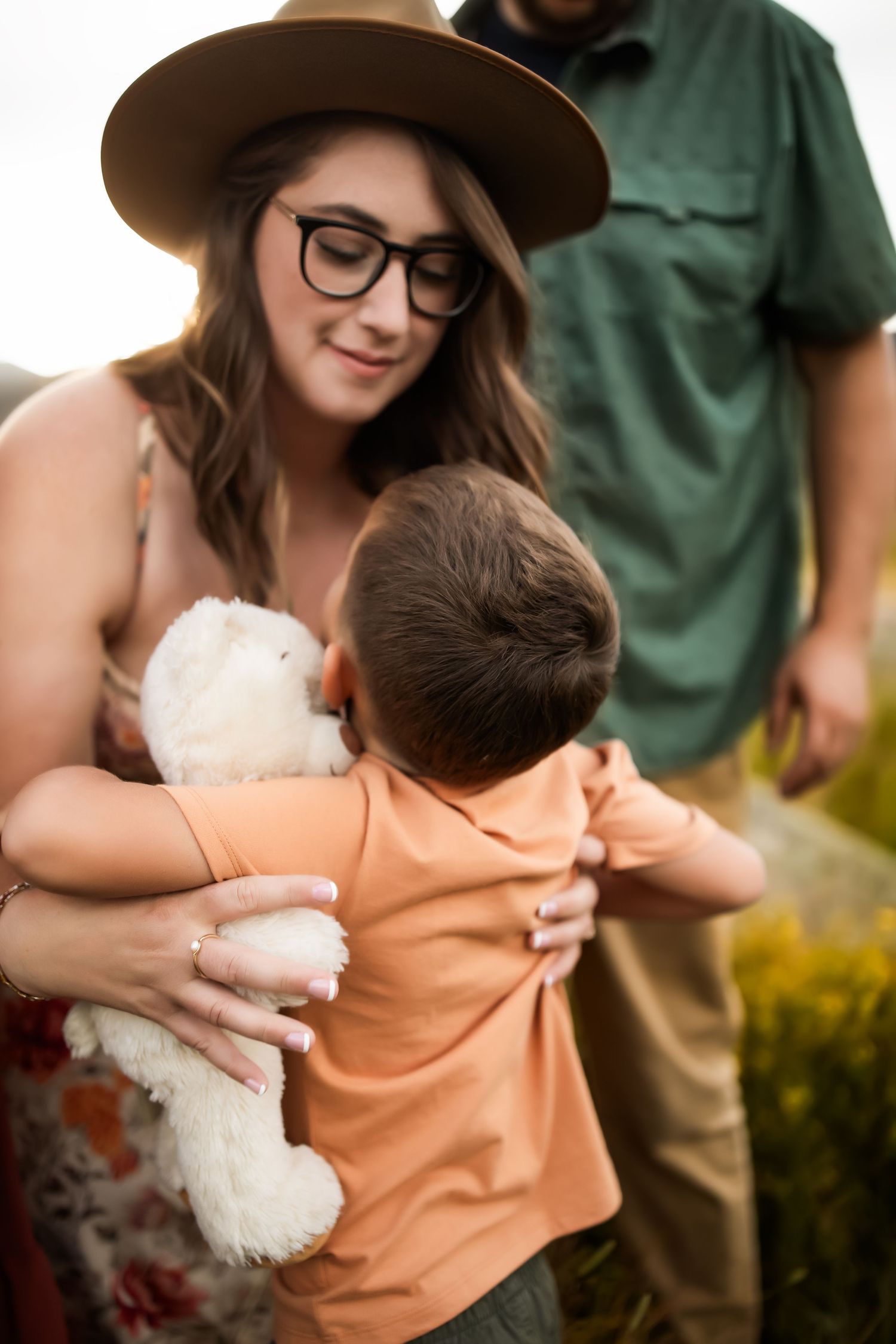 Close-up shot of a person wearing glasses and a brown hat holding a small child in an orange shirt.