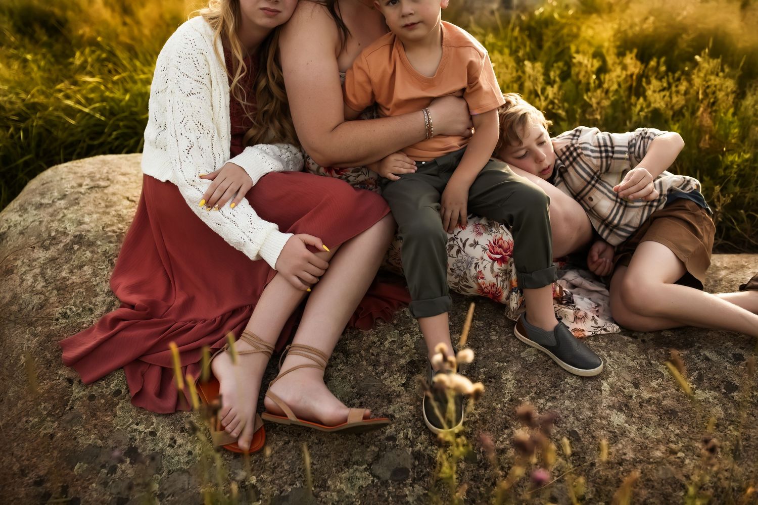 Friends relaxing together on rocks surrounded by wild grass and flowers during sunset.