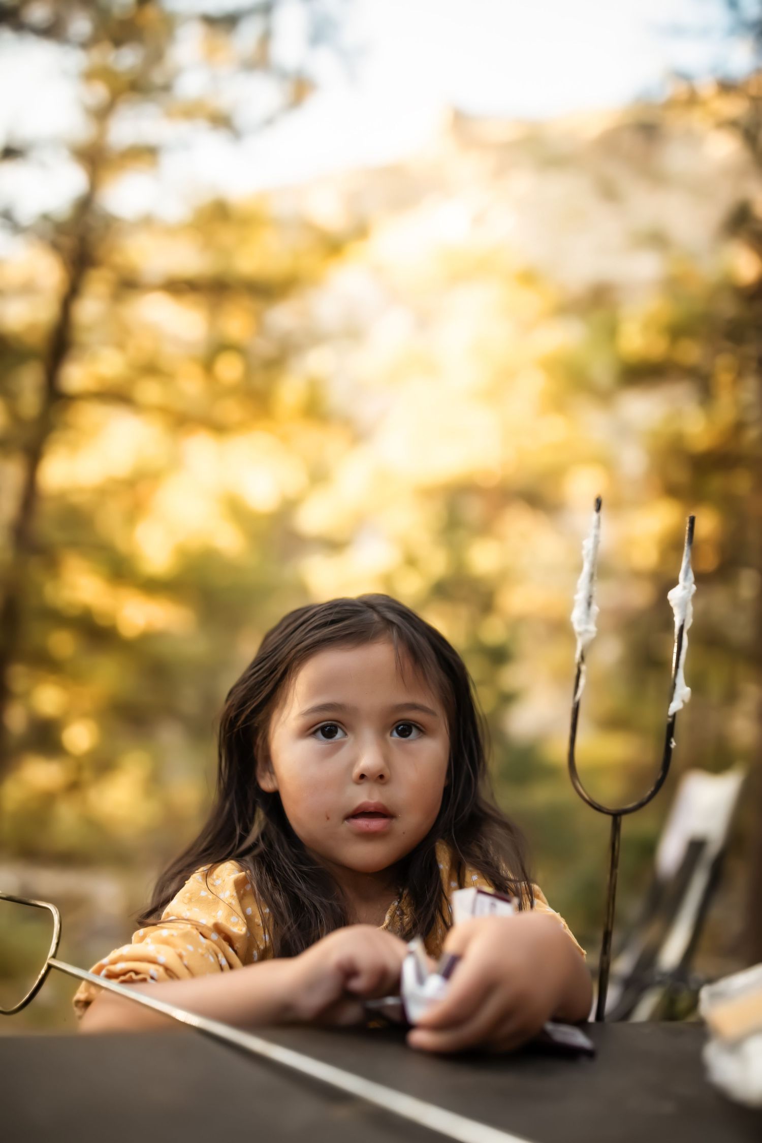 Child looking curiously at roasting marshmallow sticks during golden hour.