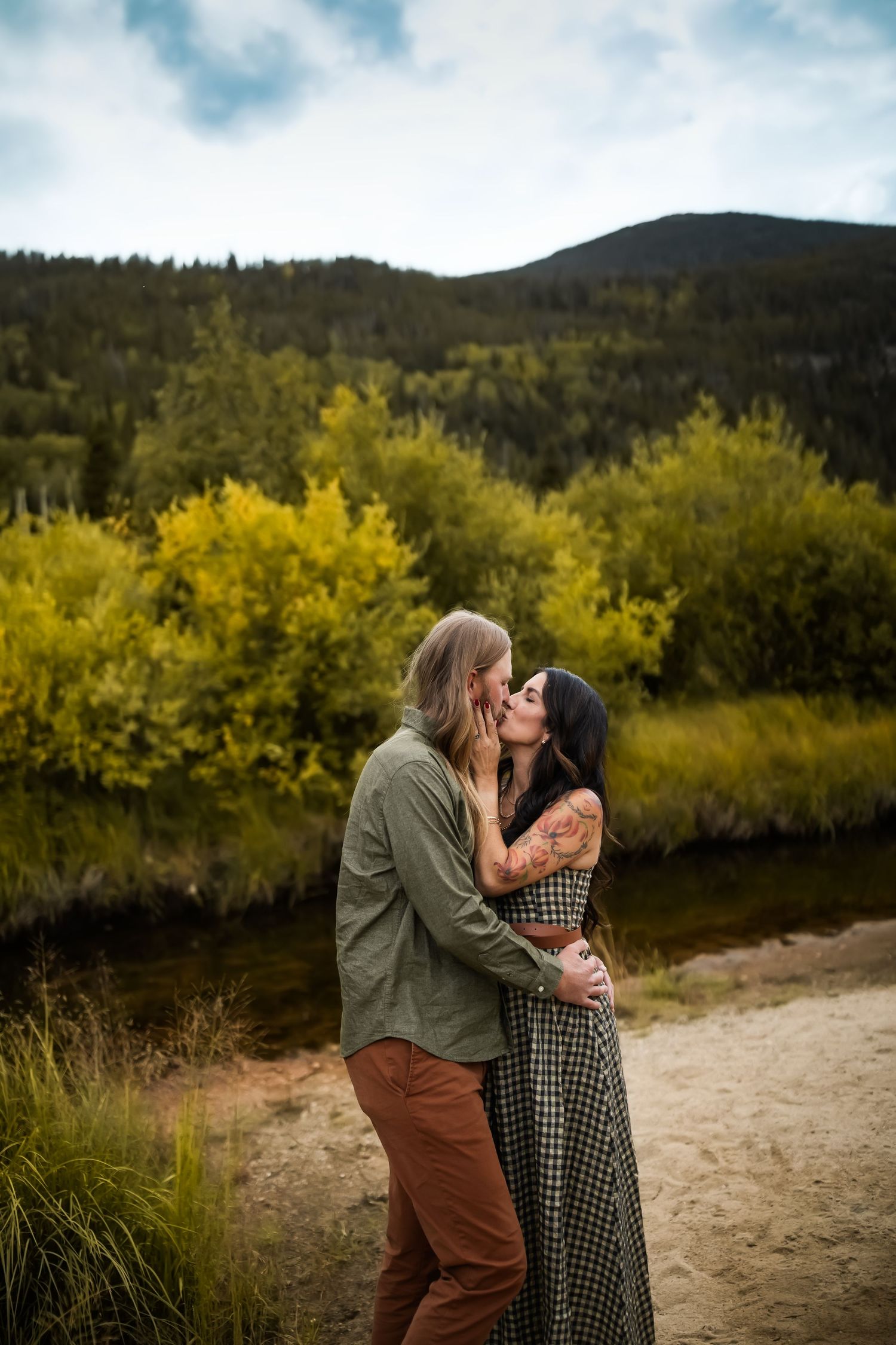 A couple shares an intimate moment against a backdrop of autumn foliage and mountains.