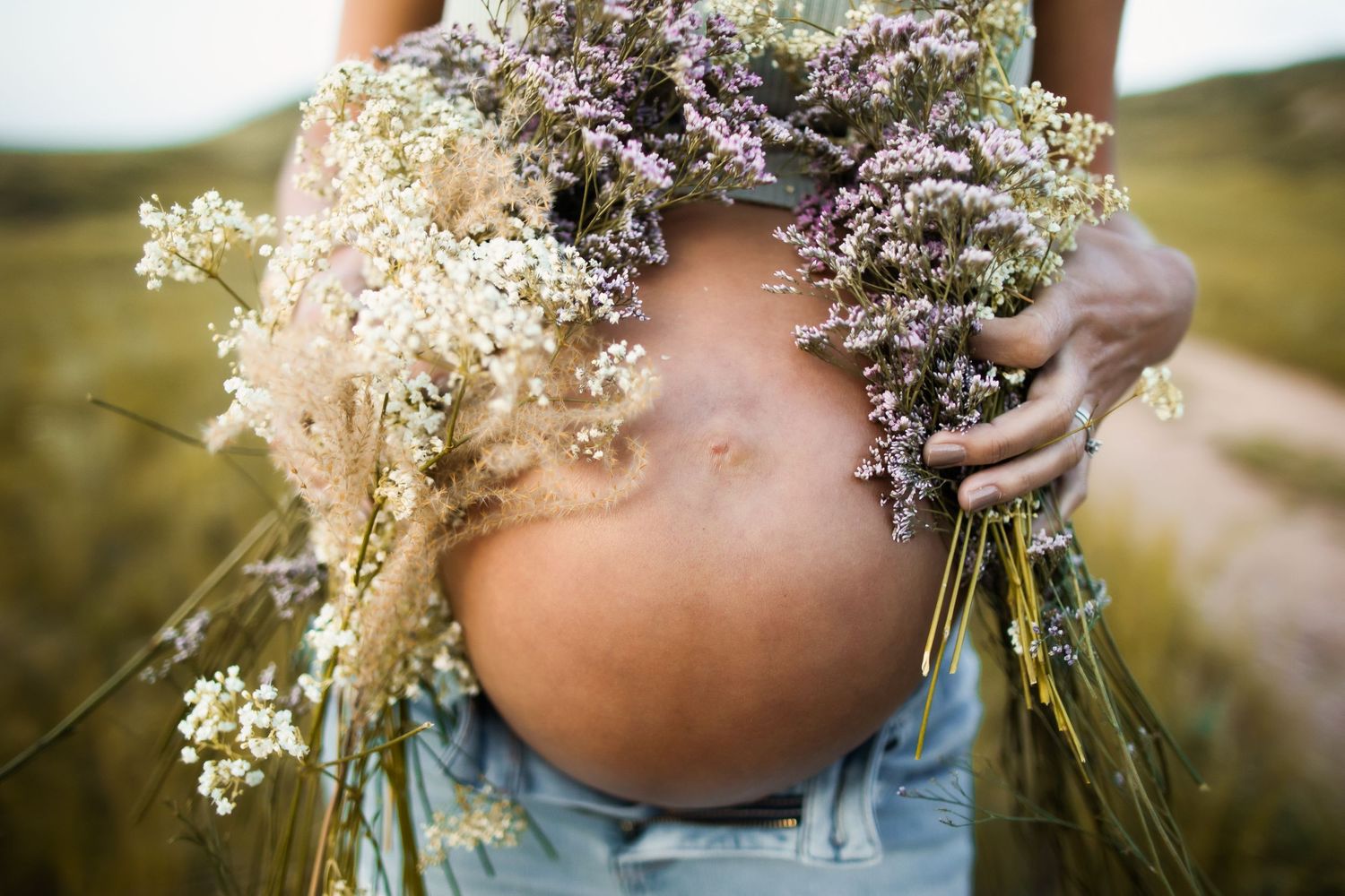 A close-up of a pregnant belly adorned with delicate wildflowers against a natural outdoor setting.