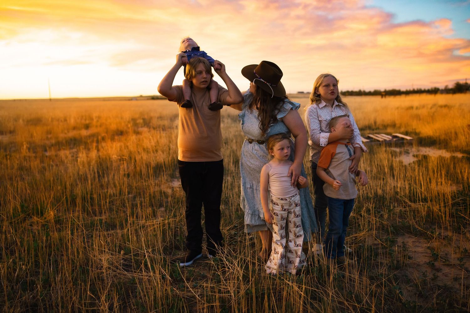 A family stands together in a golden field at sunset, creating a warm and serene scene.