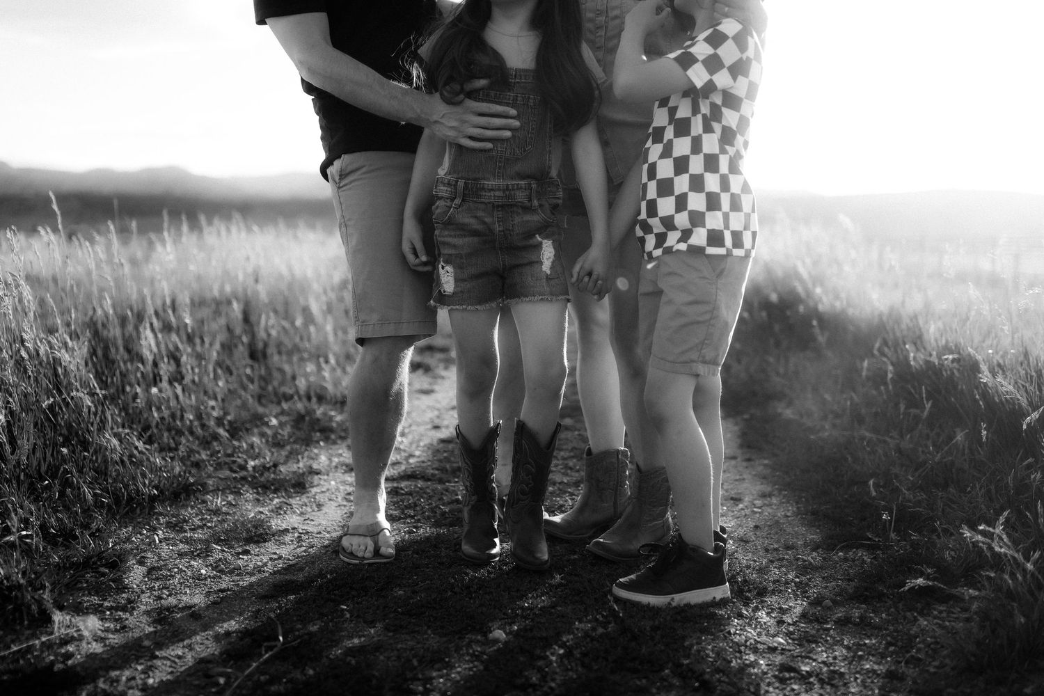 Black and white silhouette of family group embracing in a sunlit field.