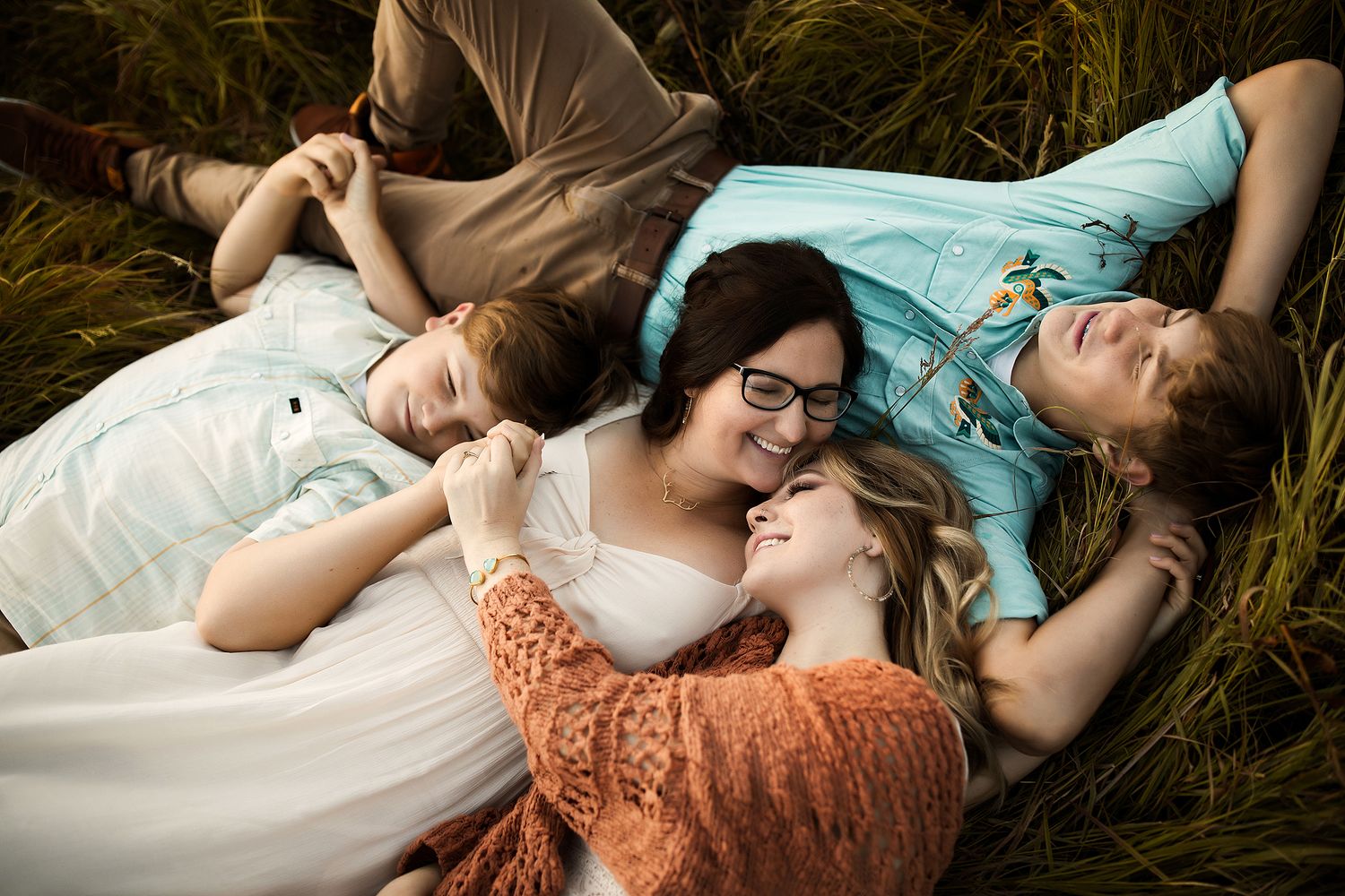 Group lying in tall grass together during golden hour creating intimate portrait.
