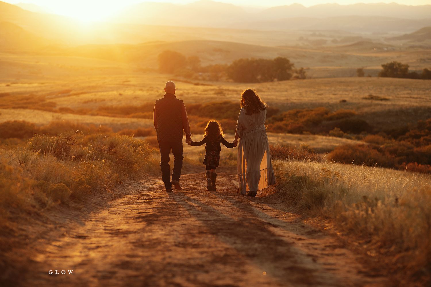 Silhouettes walking along a dirt path at sunset with golden light streaming through.