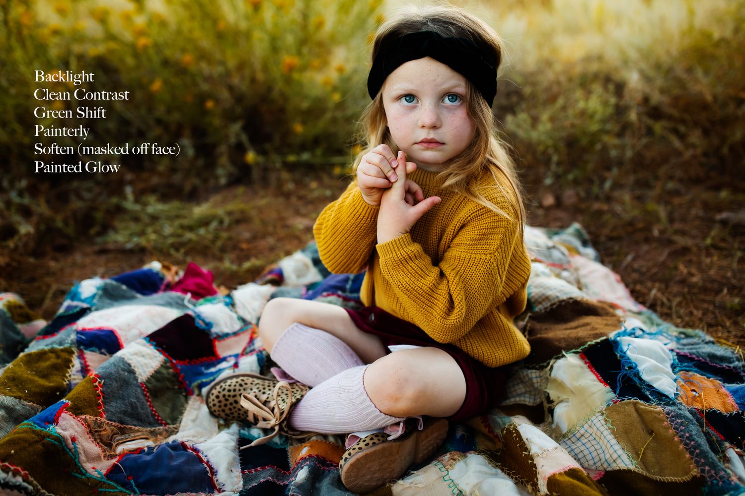 Child in mustard yellow sweater sits thoughtfully on patchwork quilt outdoors.