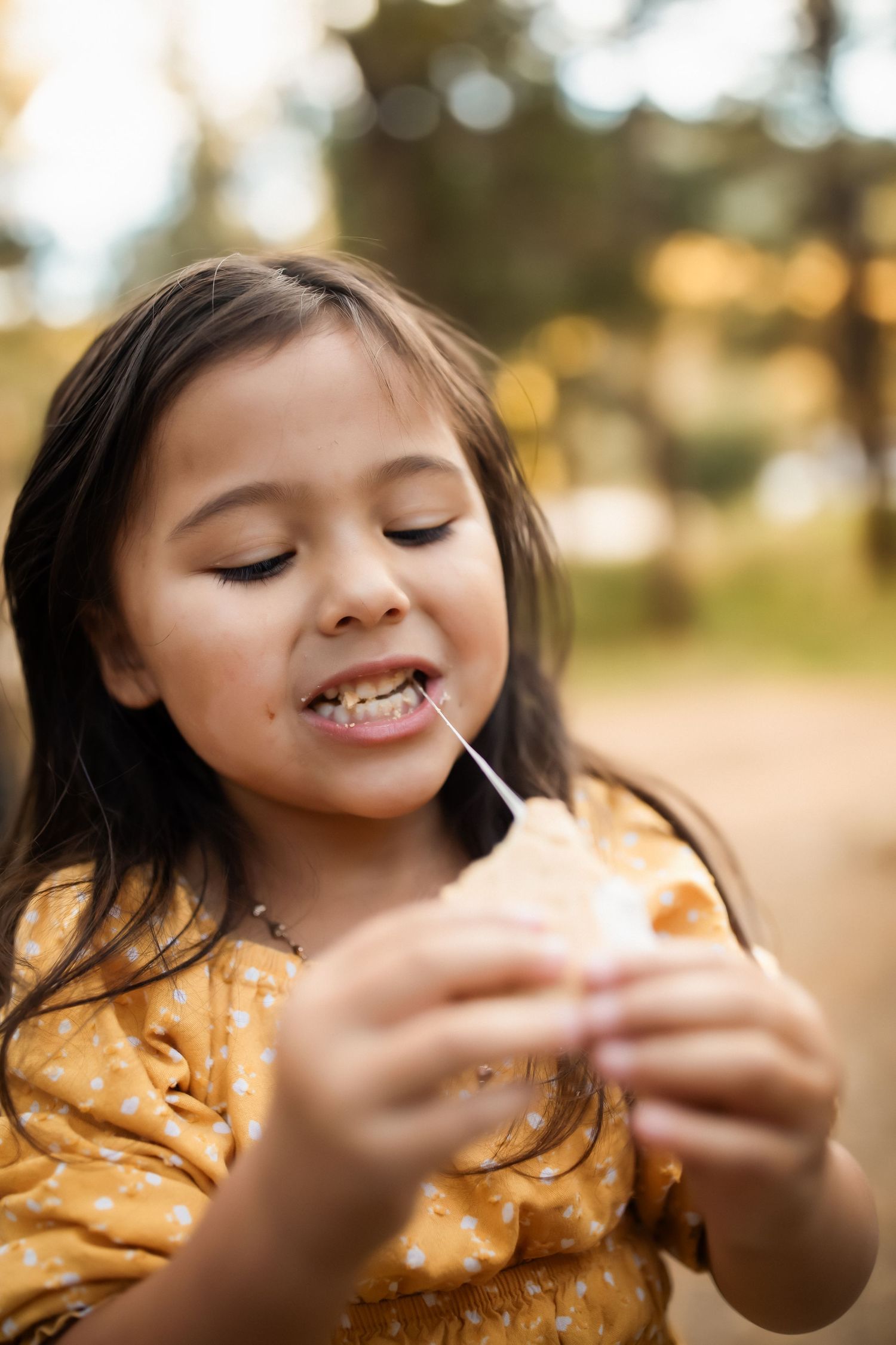Child in yellow dress enjoying a snack outdoors during golden hour.