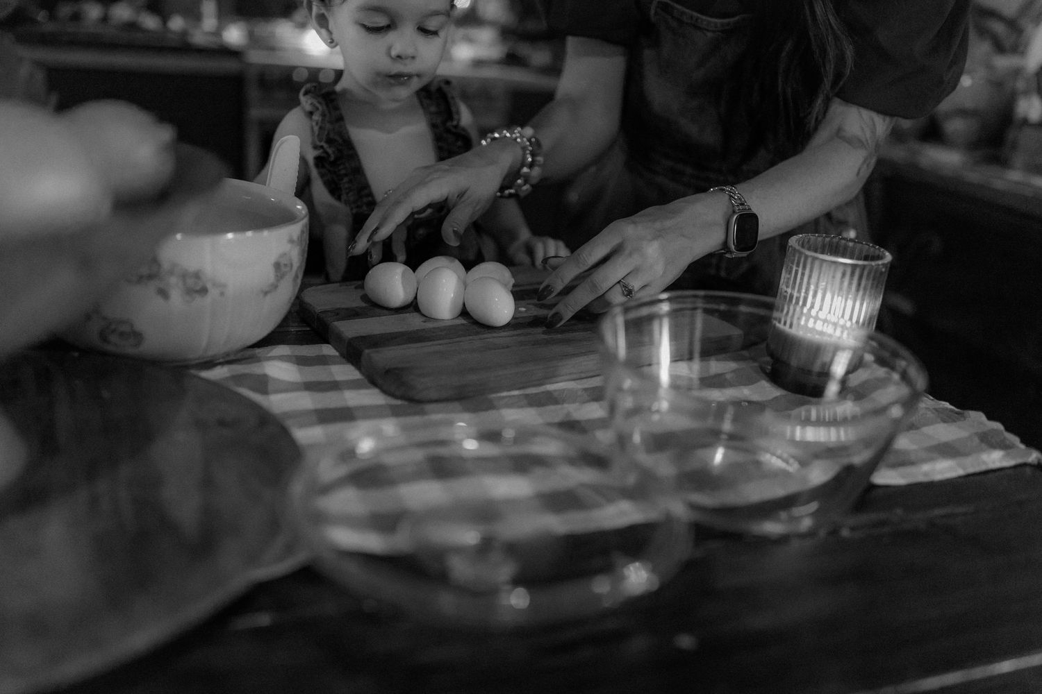 Black and white photo of a child and adult cooking together, with eggs on a cutting board and mixing bowls on a table.