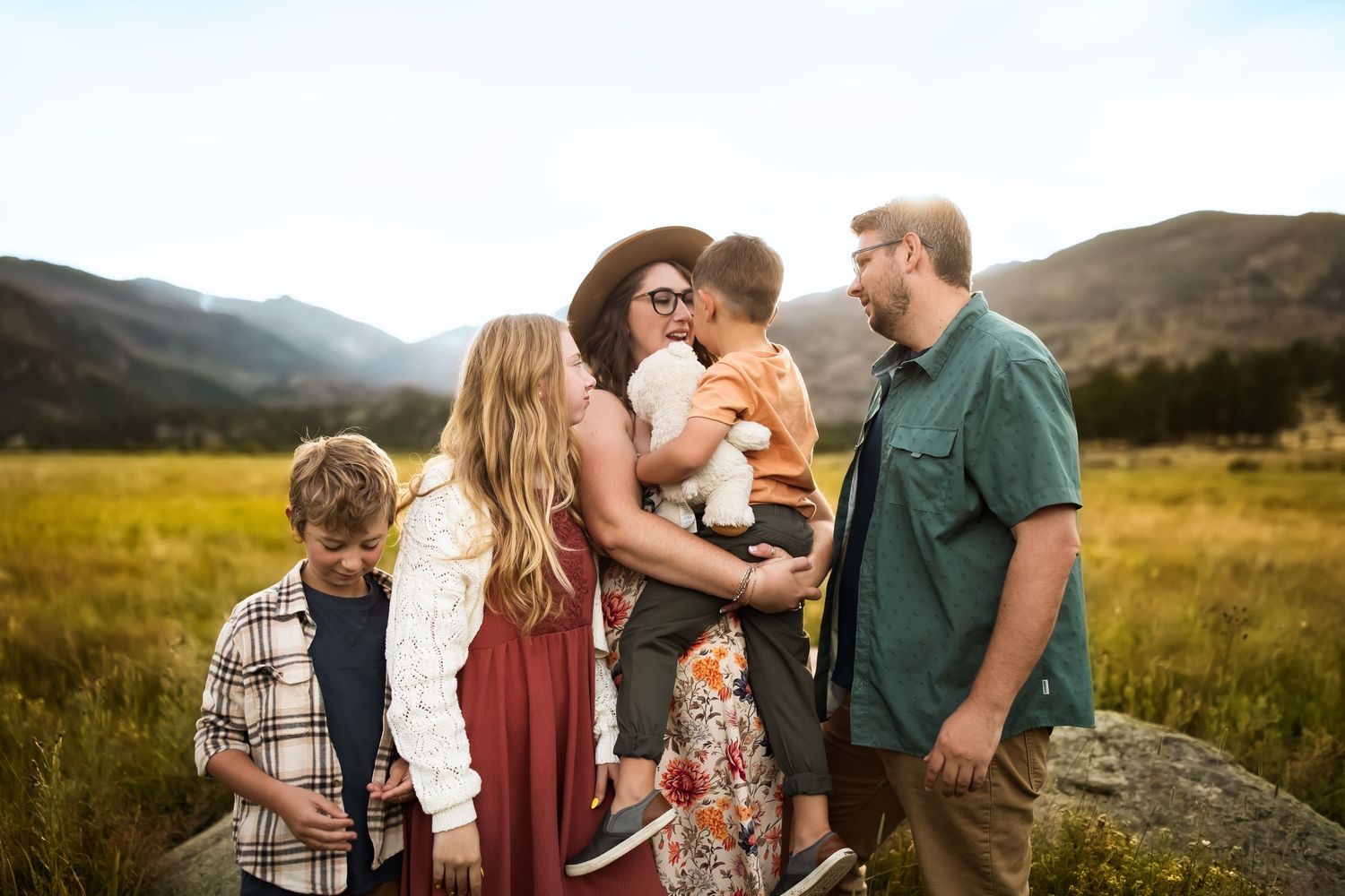 Family enjoying a tender moment together in a scenic mountain meadow during golden hour sunset.