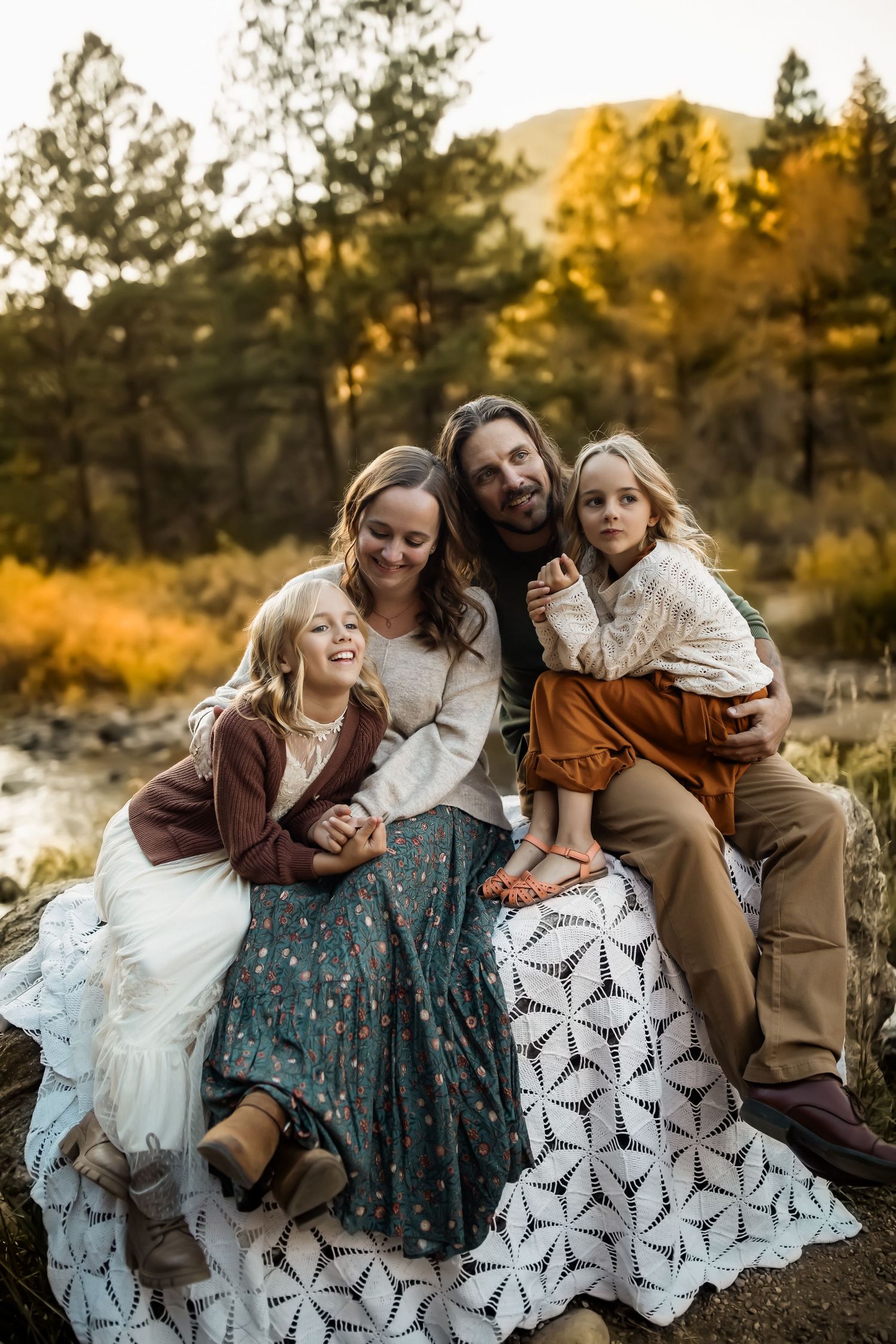 A family sitting together on a patterned blanket against an autumn mountain backdrop.