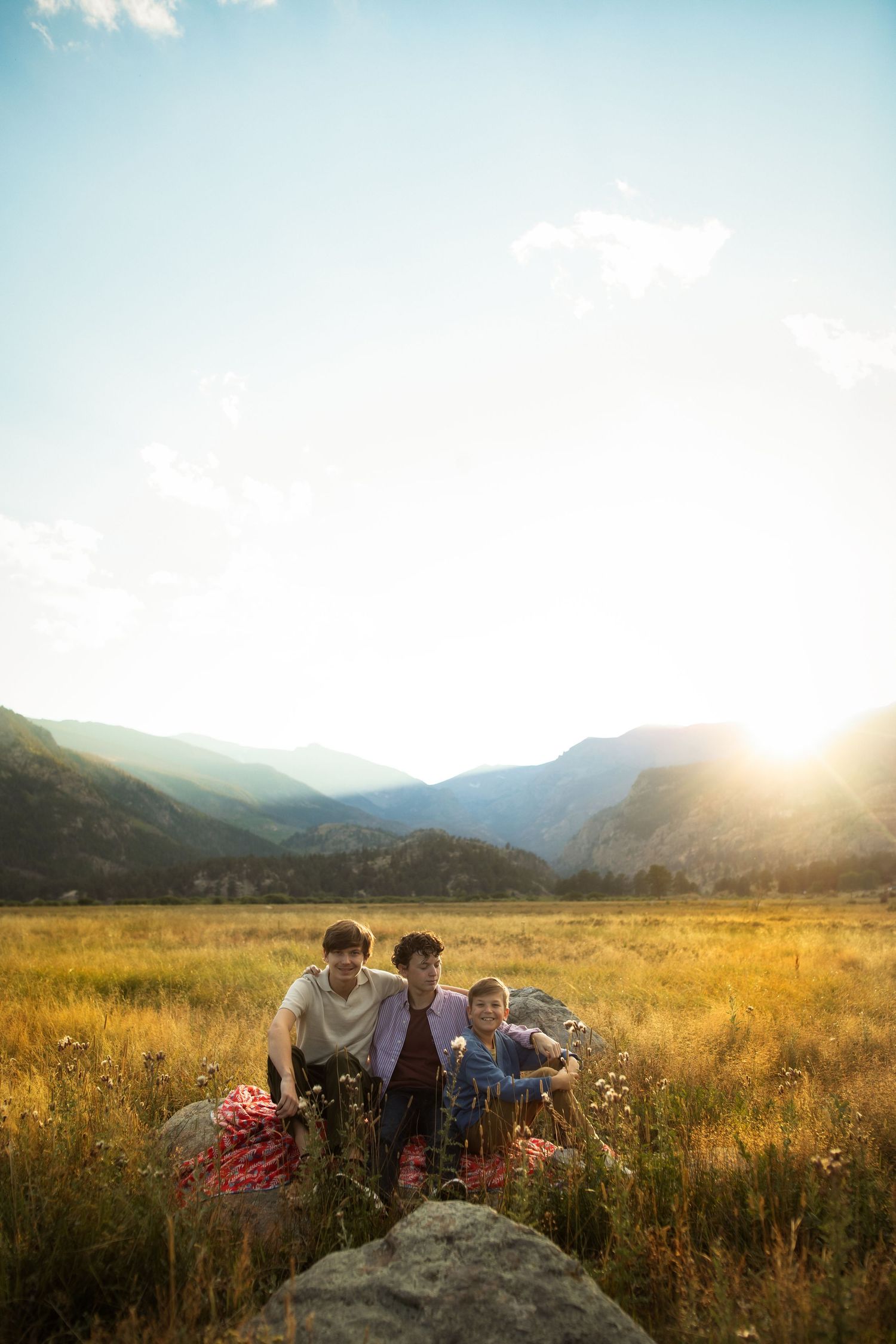 Family sitting together on rocks overlooking a scenic mountain valley at sunset.