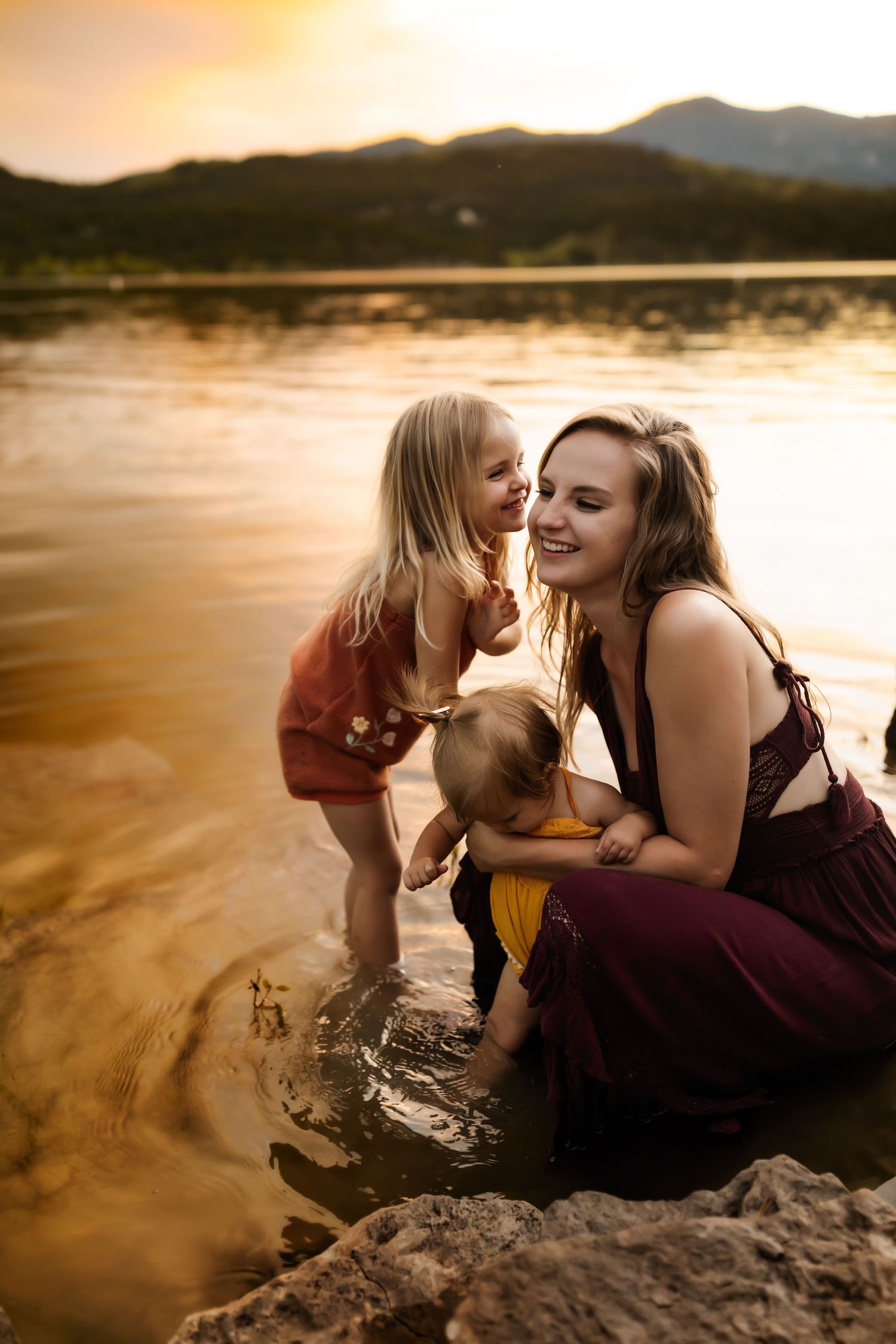 Family enjoying a sunset moment together by a mountain lake with golden light reflecting on the water.