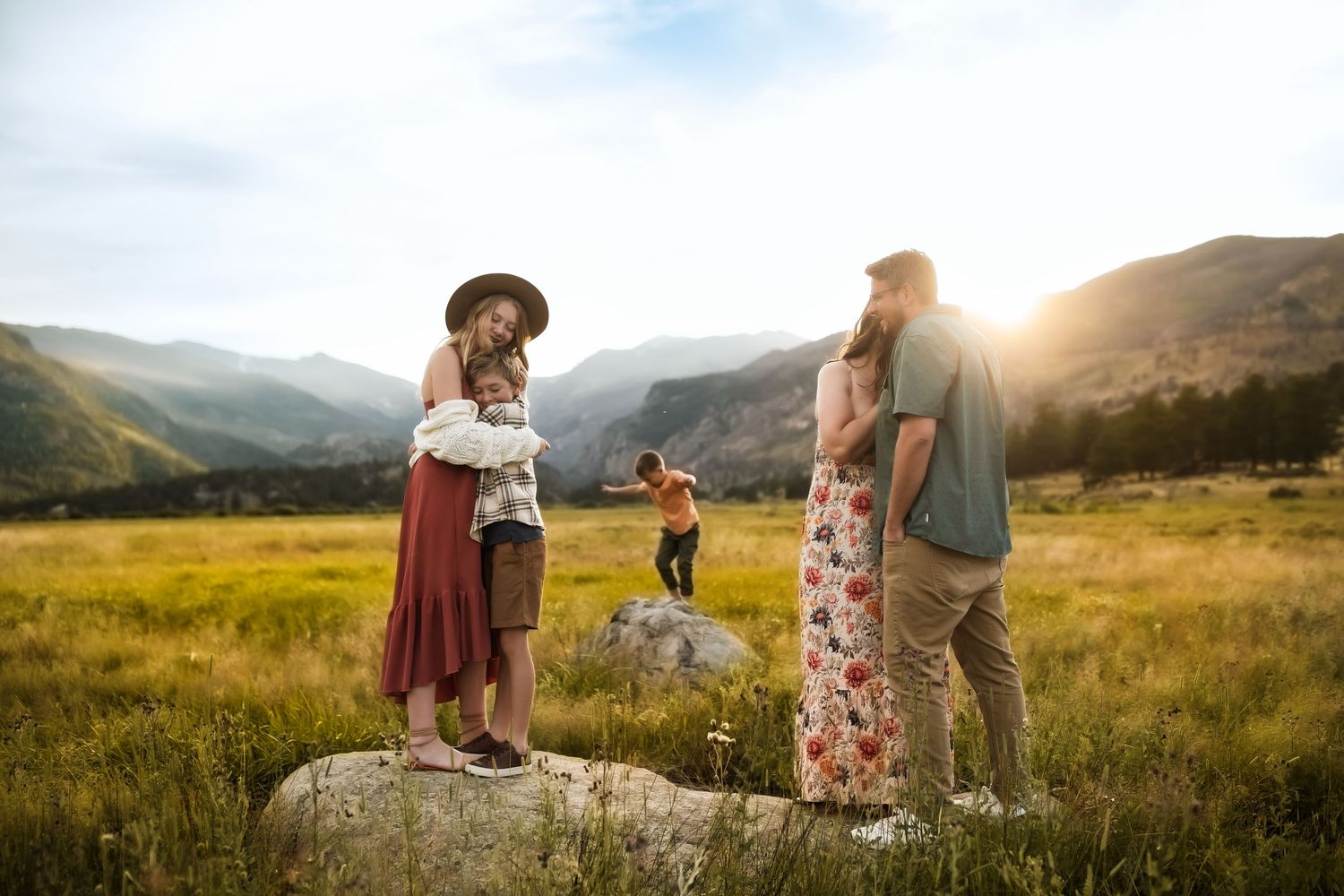 Couple embraces in a golden mountain meadow during sunset with dramatic mountain backdrop.