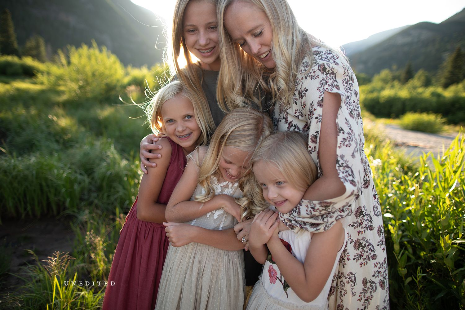 Family embracing in a golden meadow at sunset with mountains in the background.