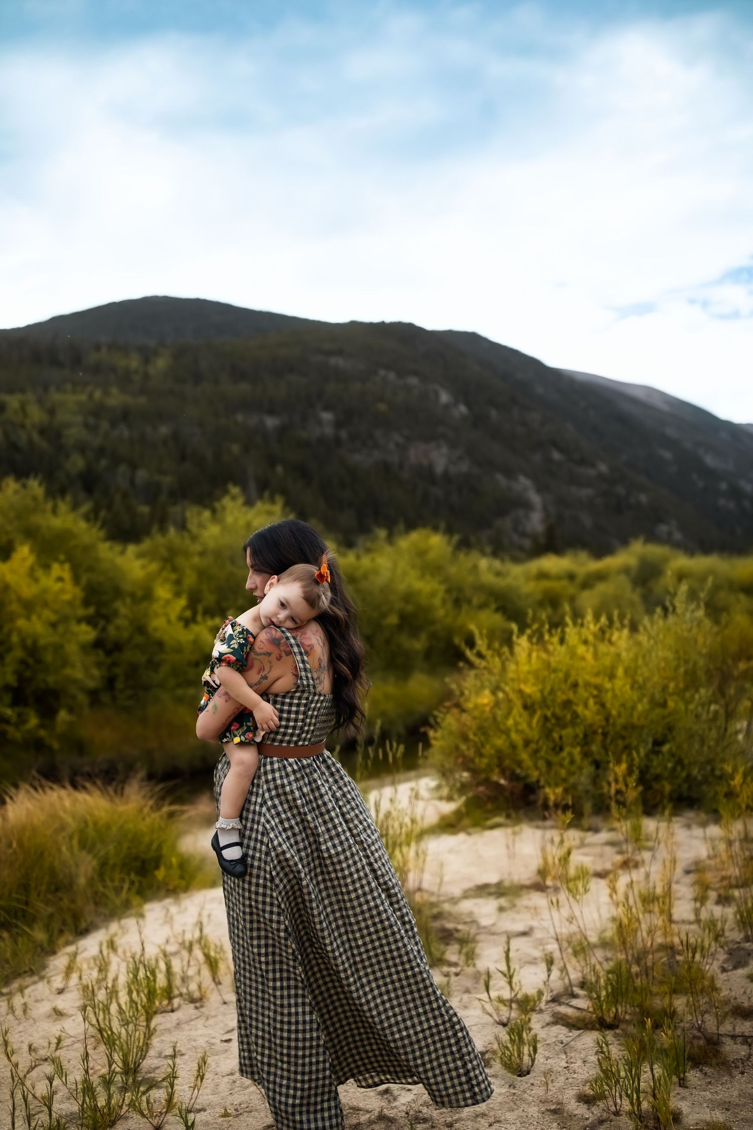 A scenic mountain landscape serves as backdrop for an intimate moment on sandy terrain.