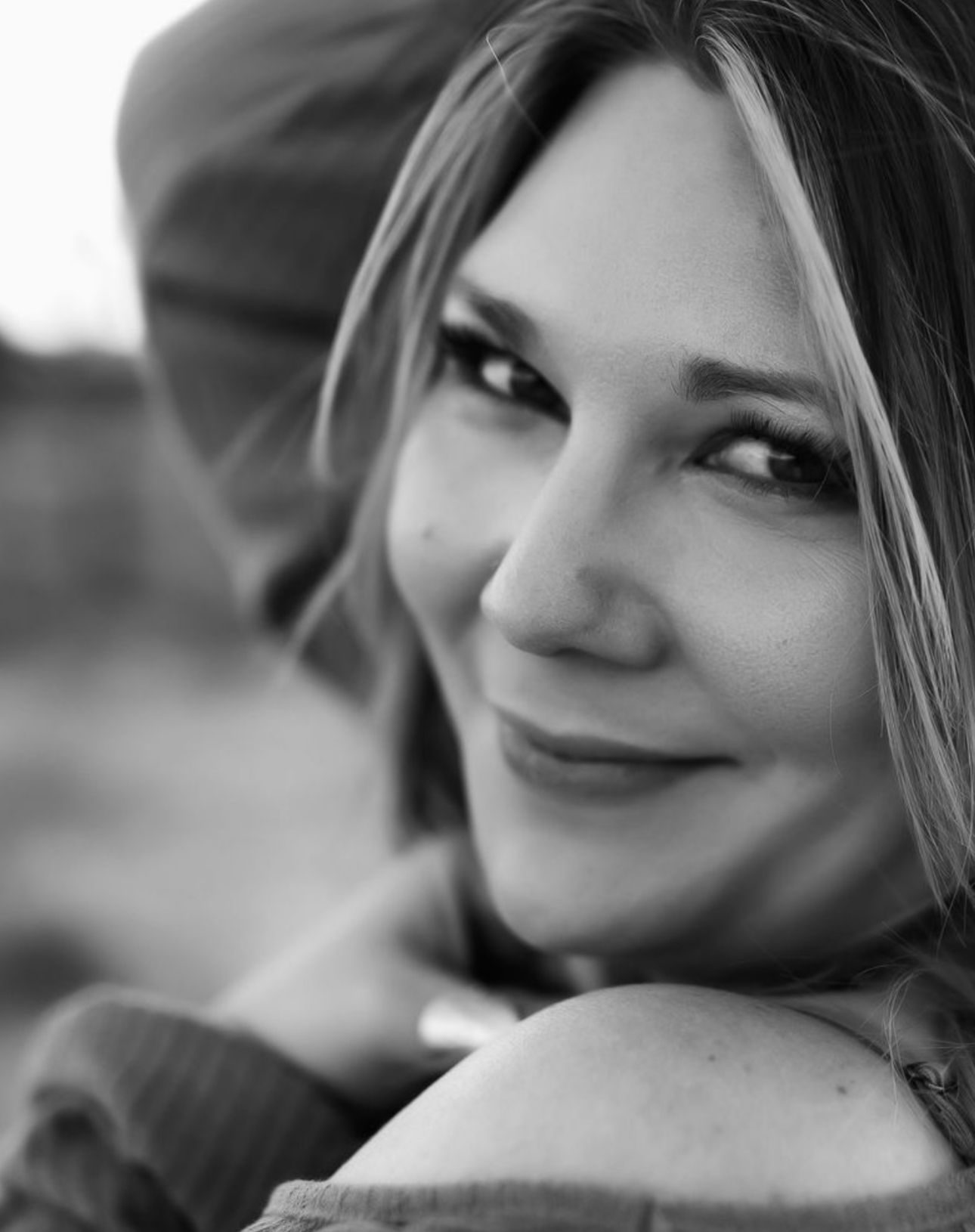 Black and white close-up portrait of a smiling blonde woman with soft lighting and blurred background.