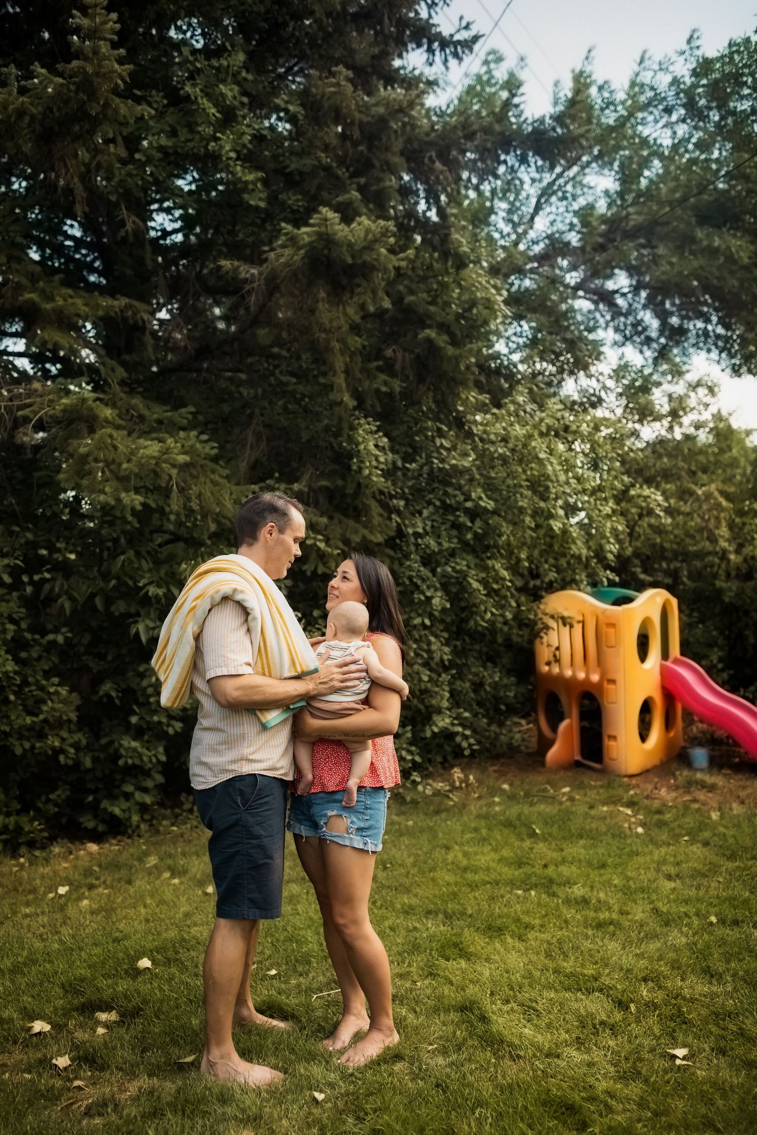A family shares an intimate moment together in their backyard with a colorful playground in the background.
