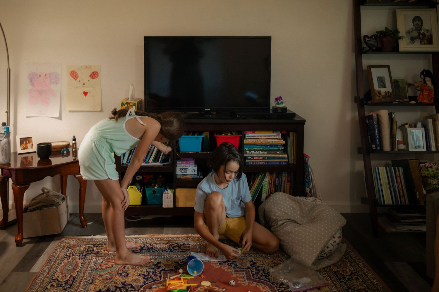 Two people playing together in a cozy living room with a TV, bookshelves, and toys on a patterned rug.