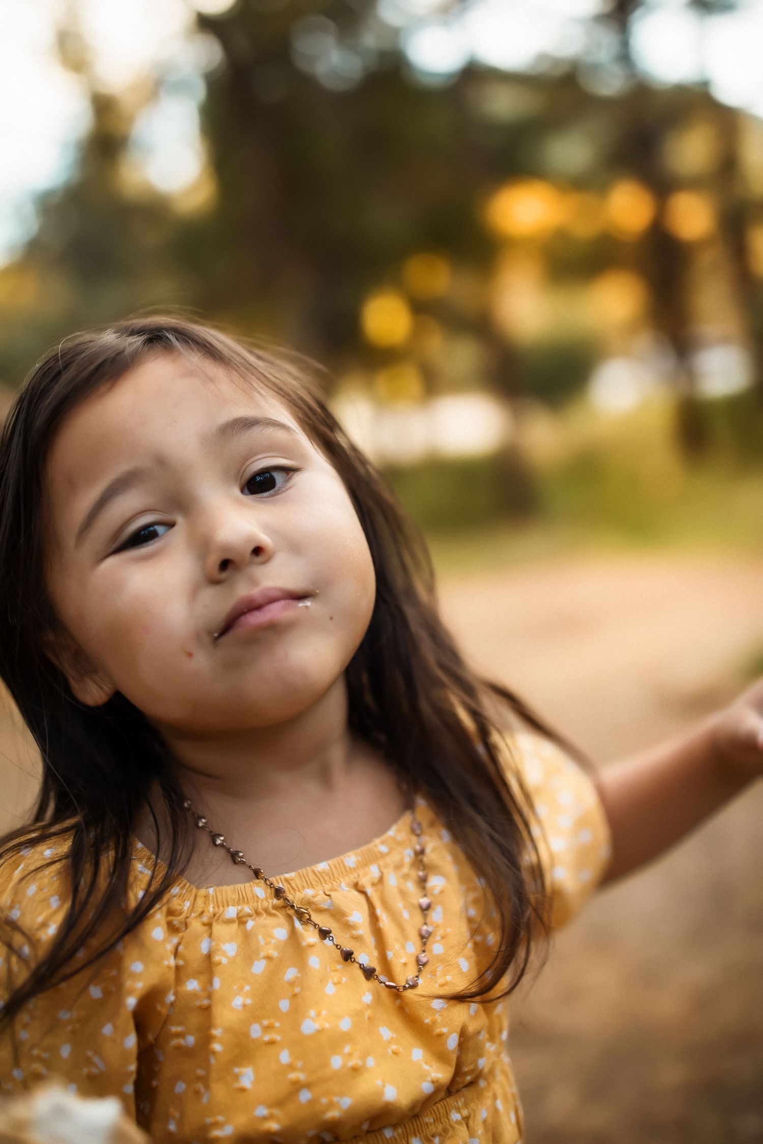 Child in yellow floral dress making silly faces outdoors during golden hour.