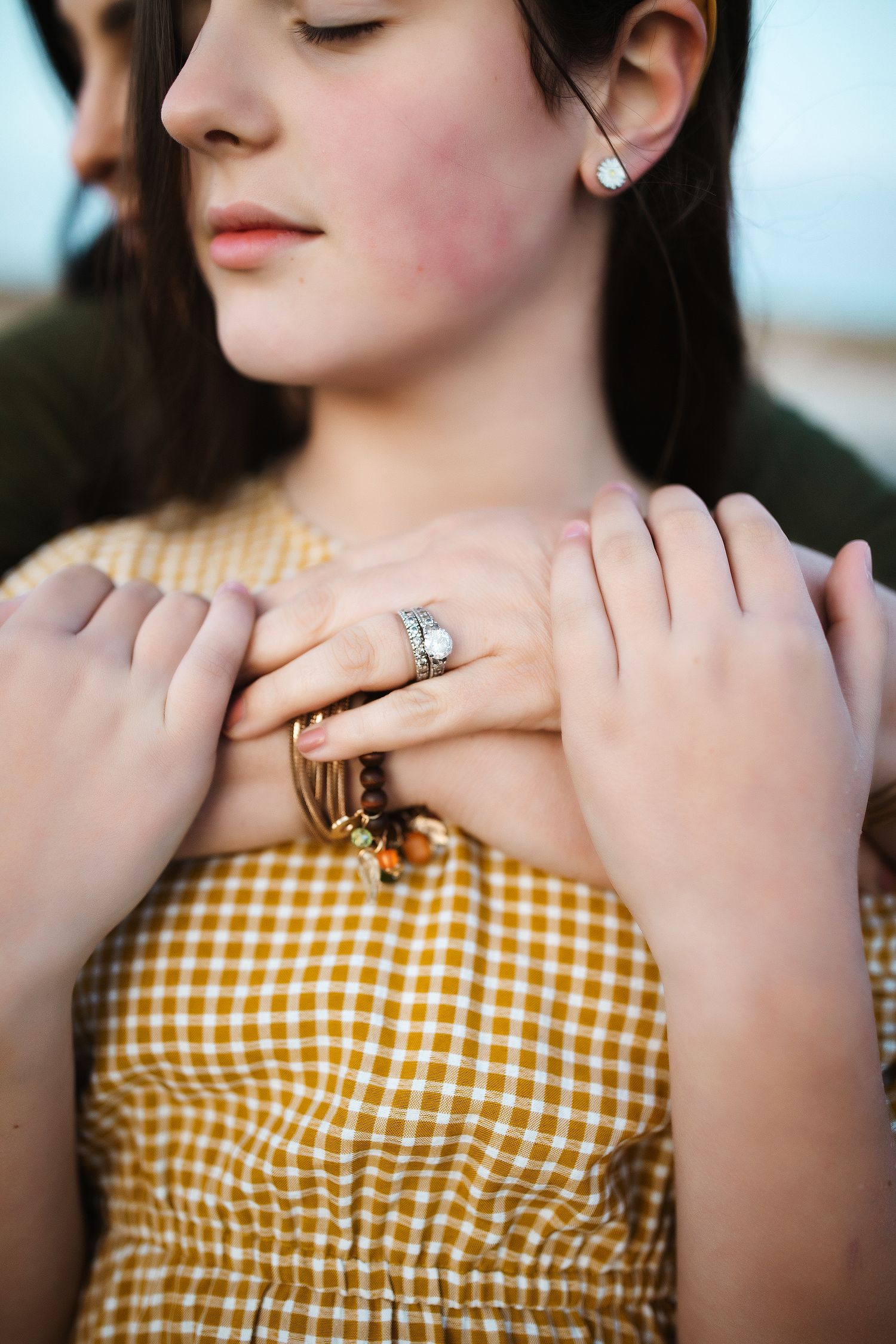 Close-up of hands with a ring resting on a yellow gingham dress.