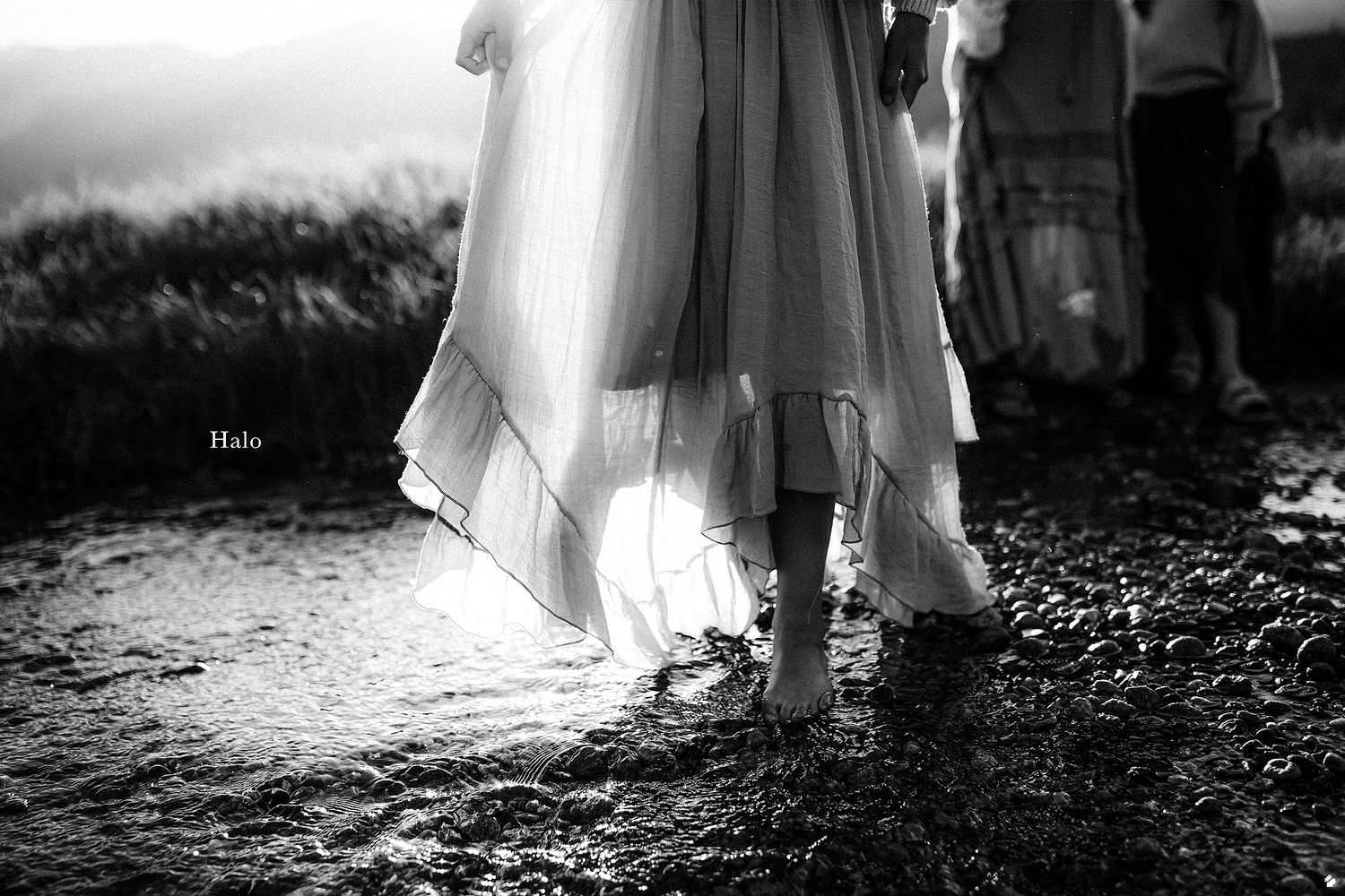 Black and white photo showing dress details and feet on rocky beach.