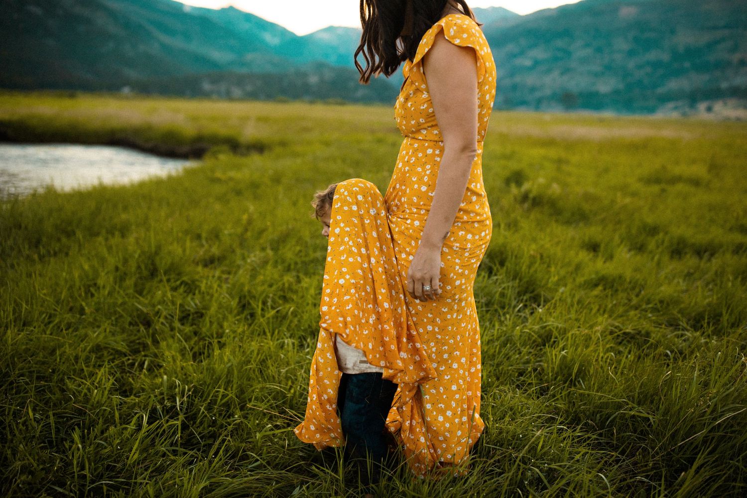 Woman in yellow polka dot dress poses in mountain meadow.