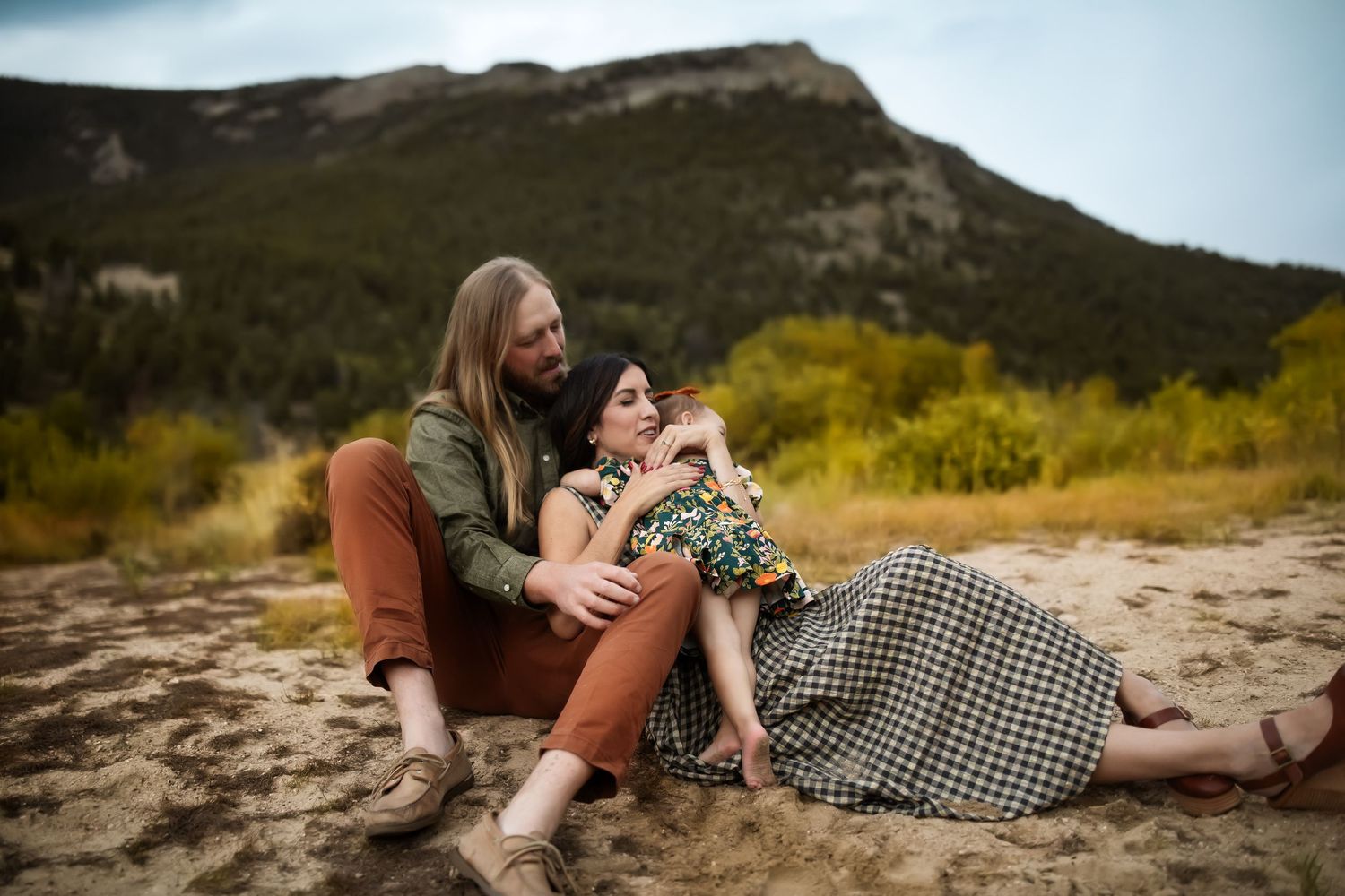 A couple shares a romantic moment while lying on rocks in a scenic mountain landscape at sunset.