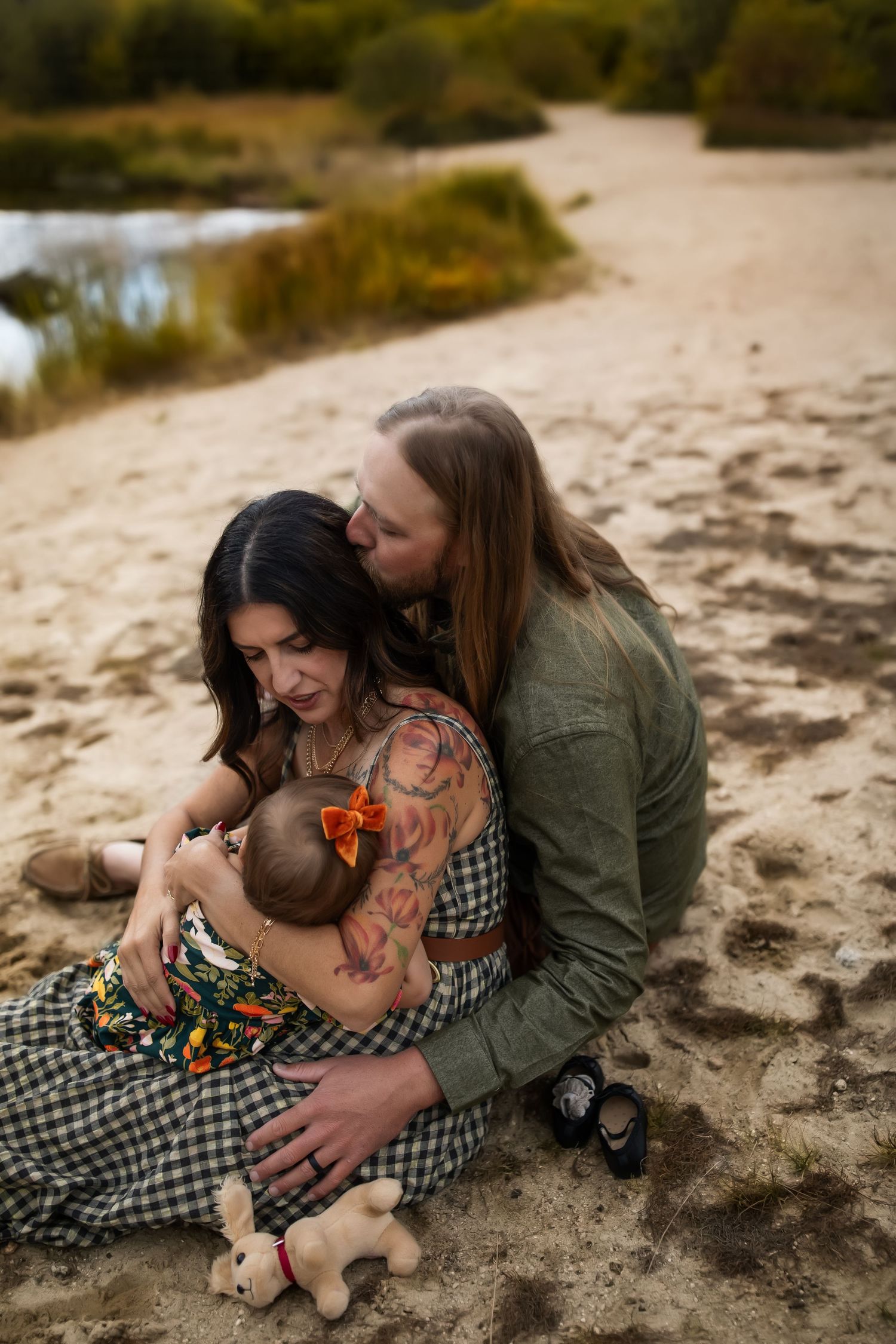 A tender family moment captured on sandy terrain with mountains and greenery in the background.