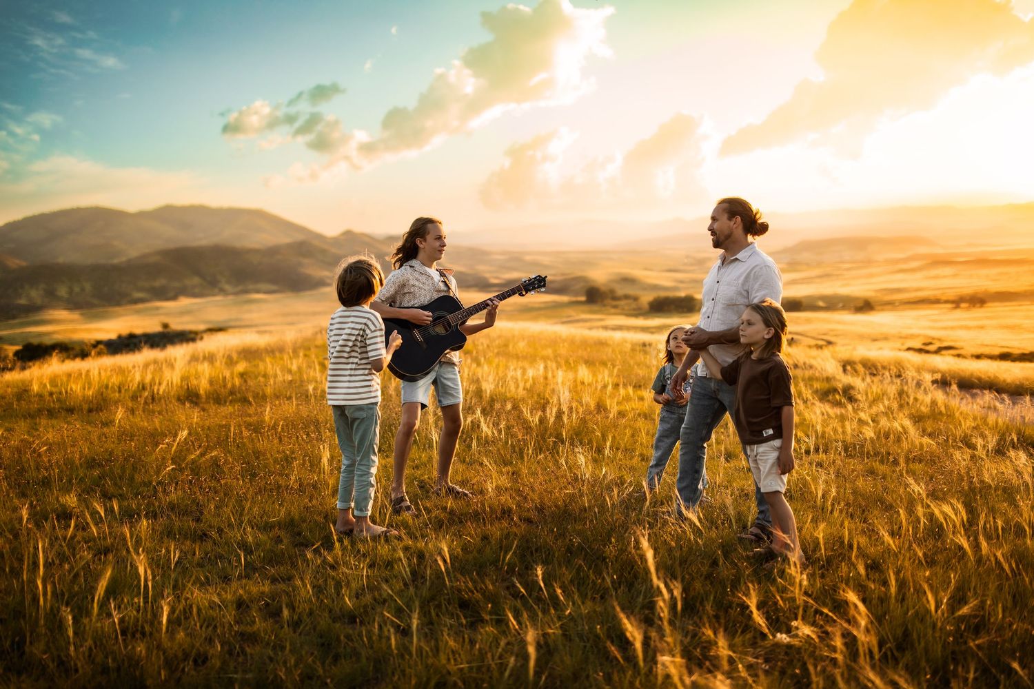 Two people dance and twirl through a golden wheat field at sunset while mountains rise in the background.