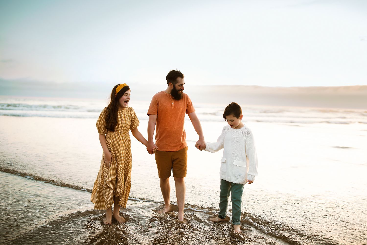 Family walks along scenic beach shoreline at sunset with waves gently rolling in the background.