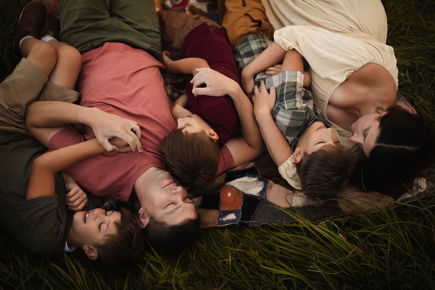 Group of friends lying on grass together, laughing and enjoying a relaxed outdoor gathering on a summer day.