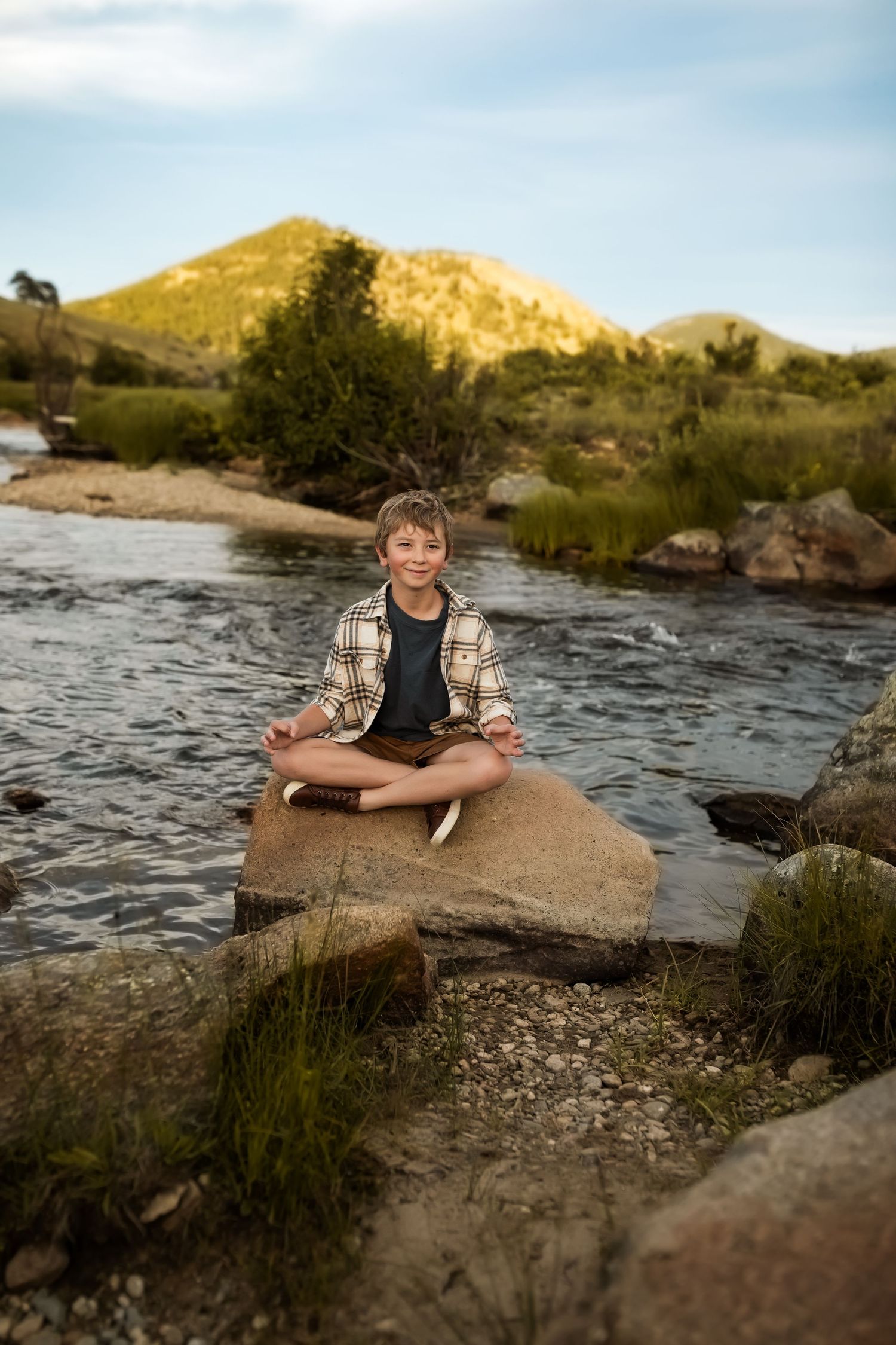 Someone resting on rocks by a flowing river with mountains in the background during golden hour.