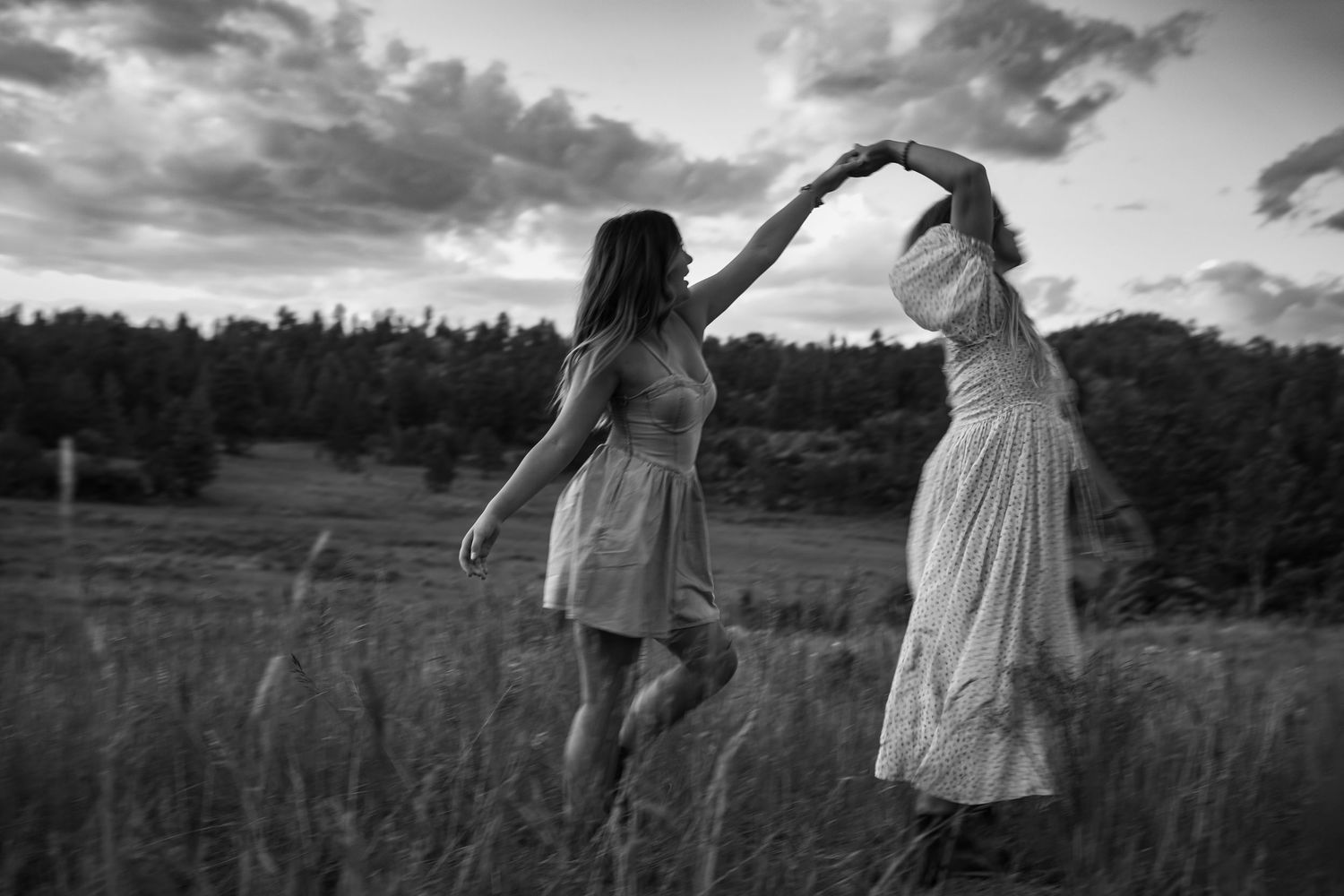 Two people in light dresses dance together in a grassy field at dusk in black and white.