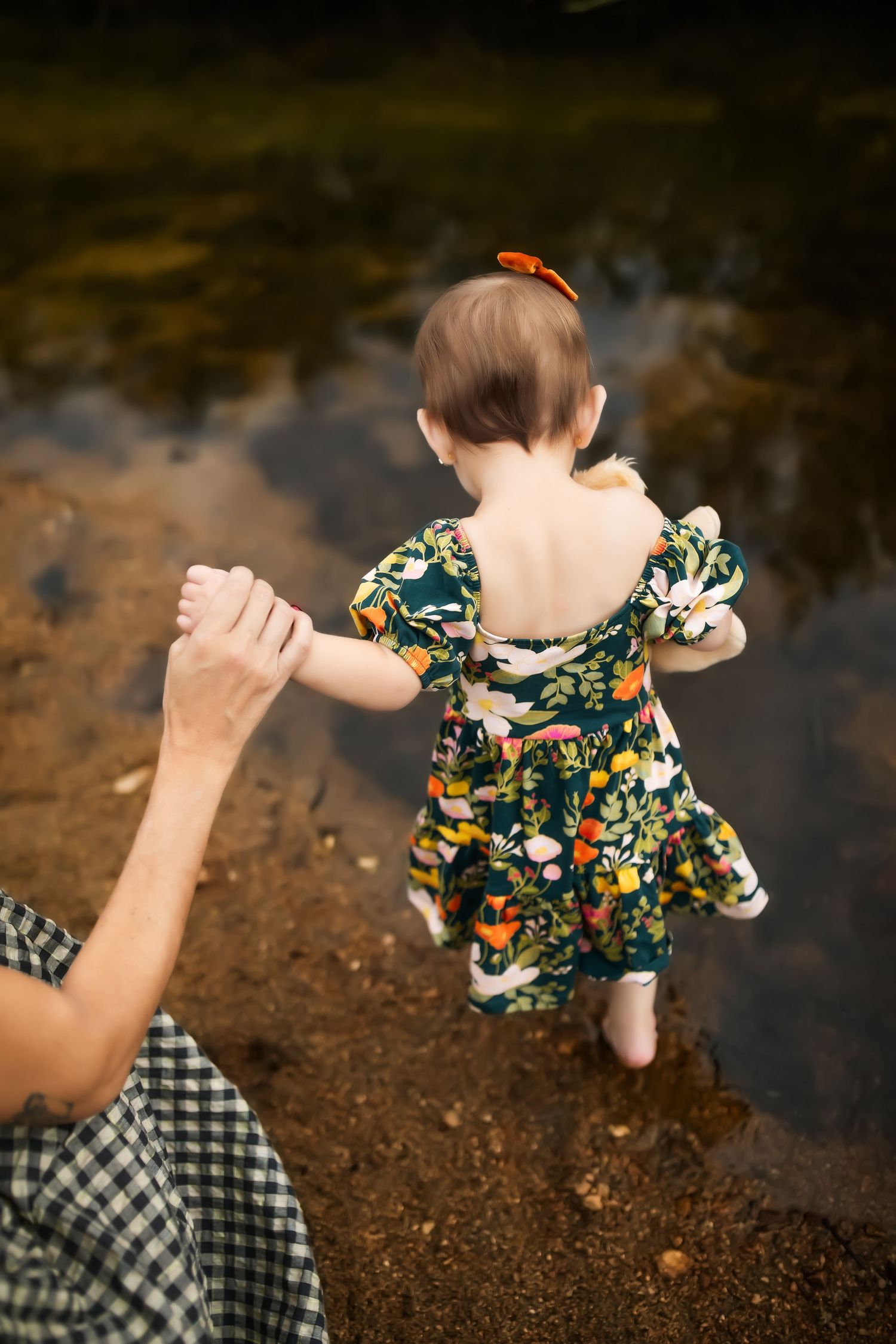 Child in floral dress plays by a reflective pond on a sunny autumn day.