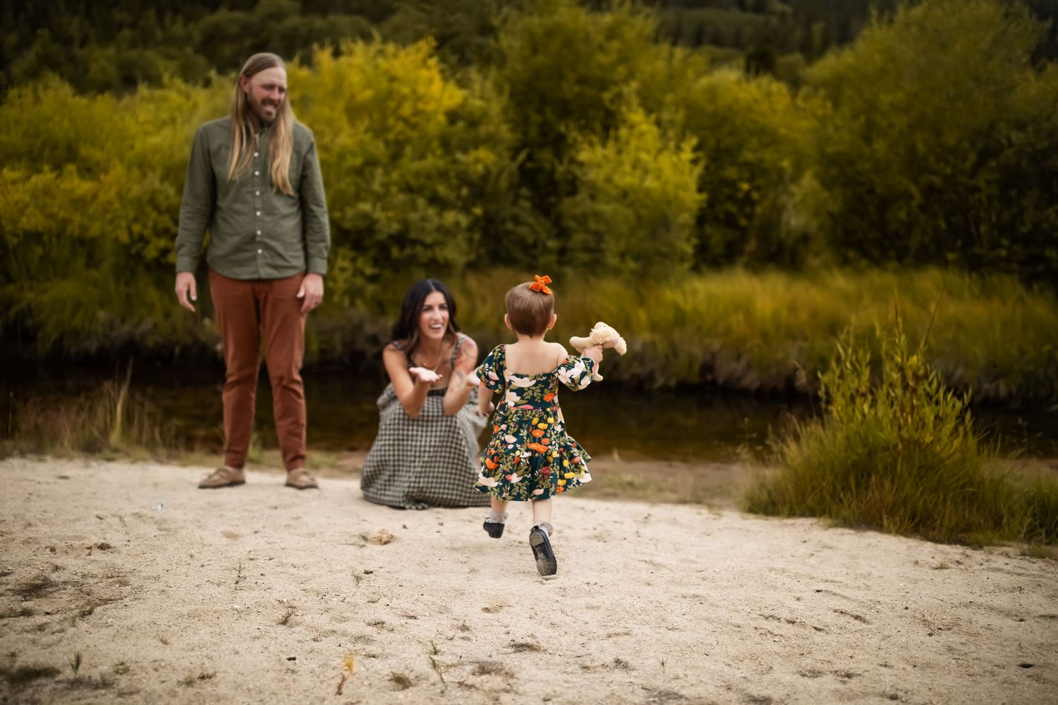 A family and their dog enjoy a playful moment together on a sandy beach path surrounded by lush greenery.