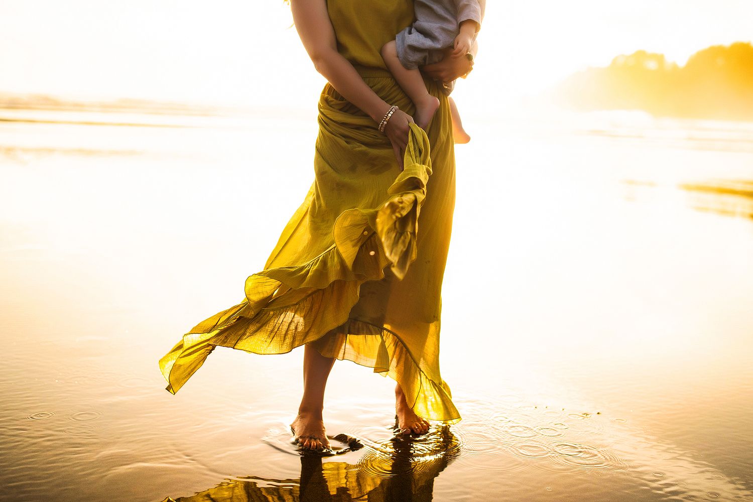 Person in a flowing yellow dress twirling by the water during golden hour.