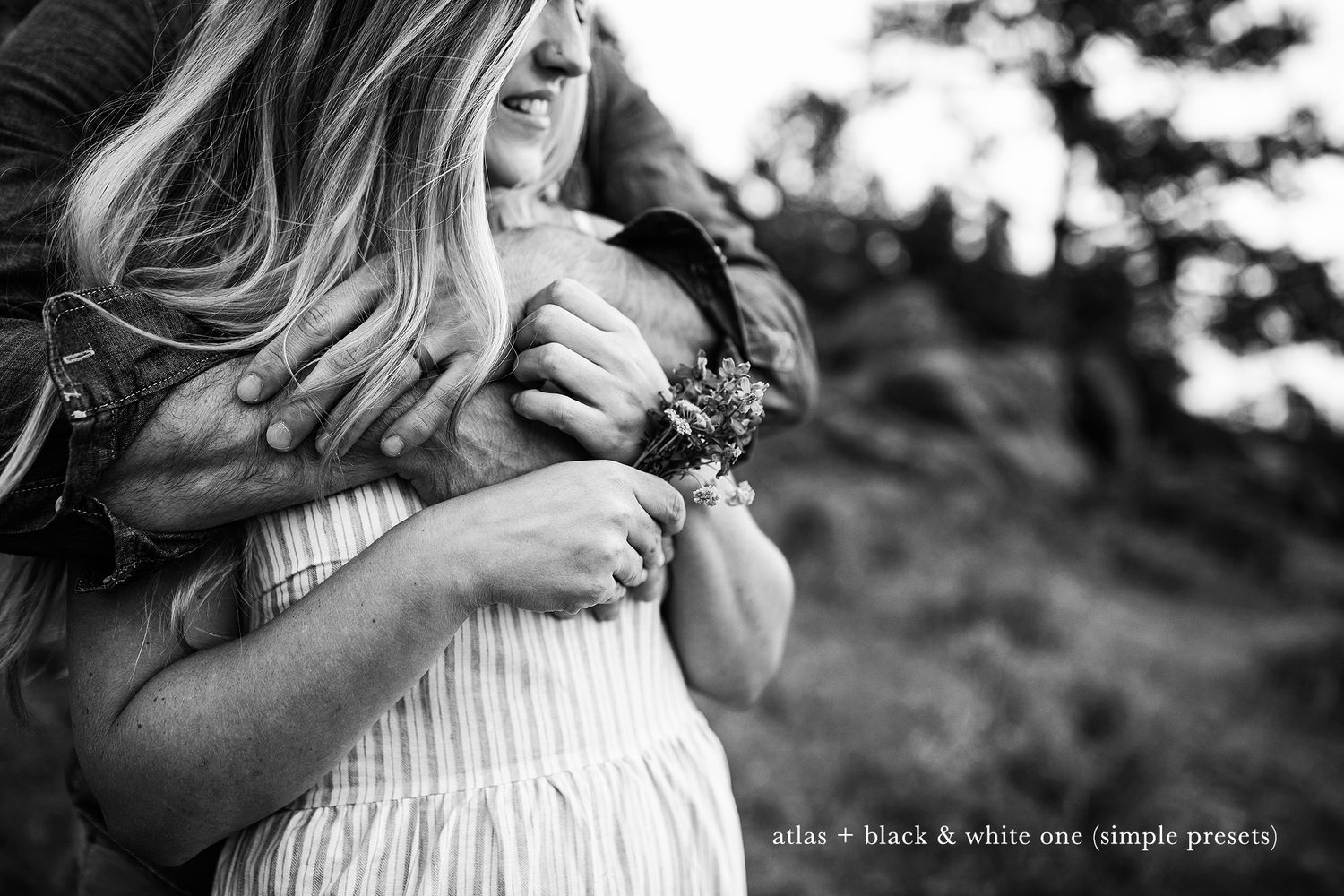 Black and white portrait of a tender embrace against a natural outdoor backdrop.