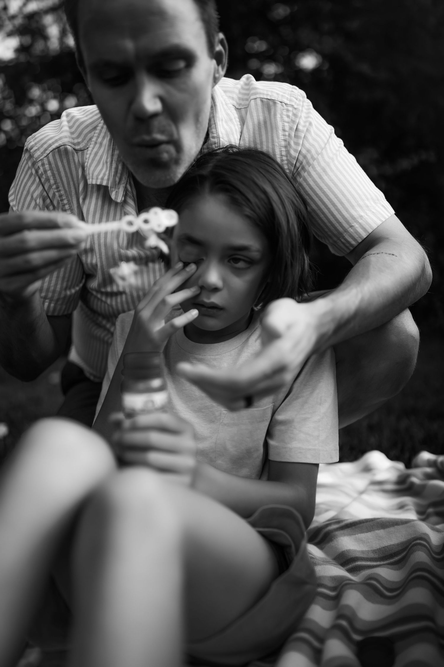 A sequence of black and white photos showing someone helping a child blow bubbles outdoors.