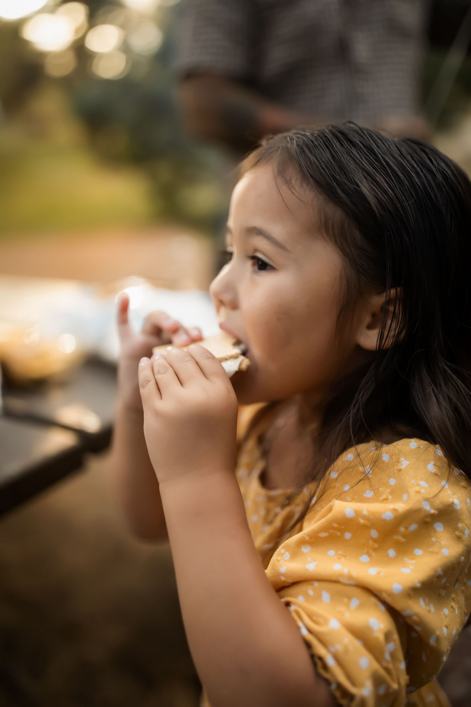 Child in a yellow polka dot dress making silly faces in warm golden light.