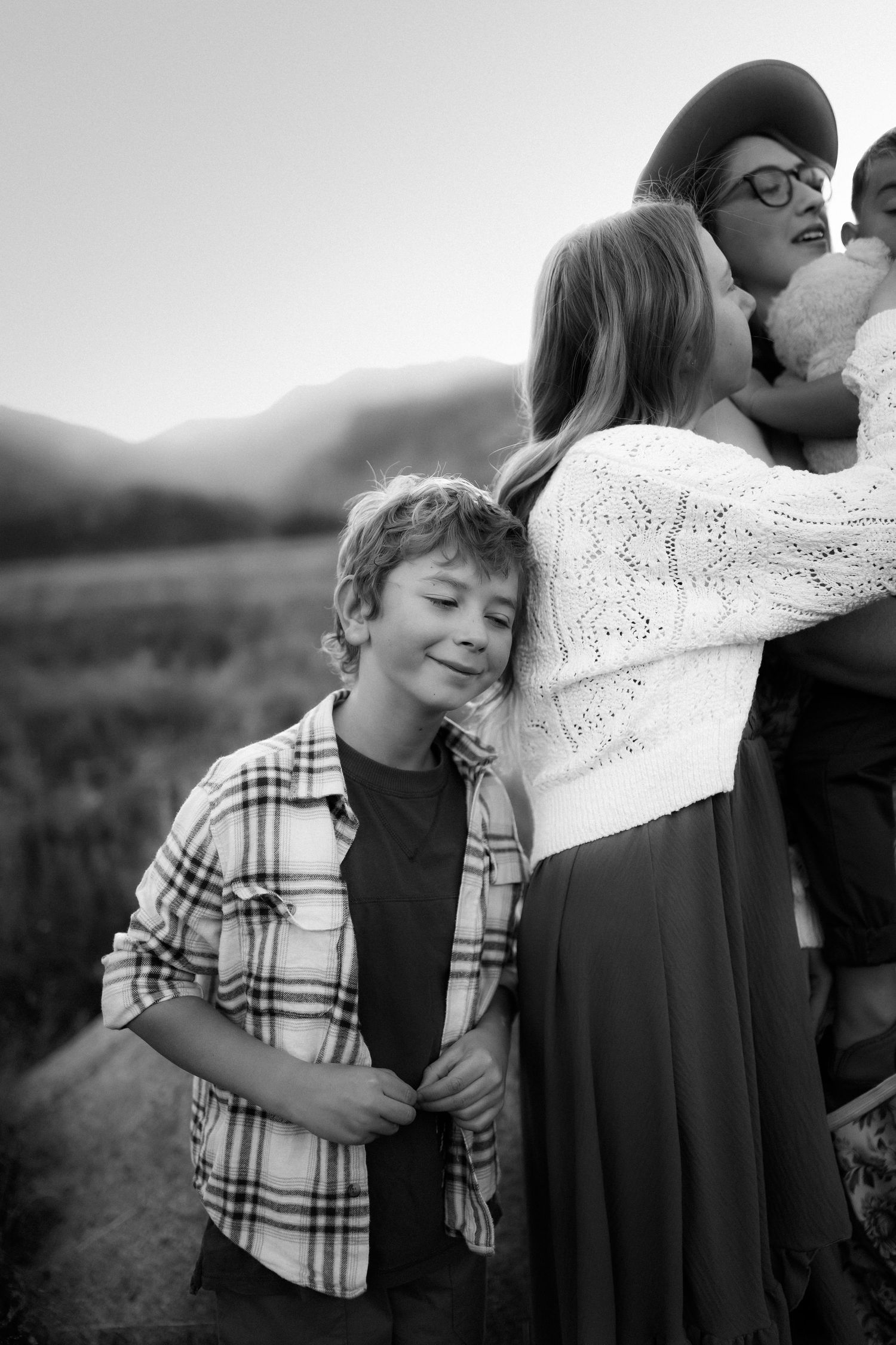 A candid black and white family portrait showing affectionate moments outdoors with mountains in the background.