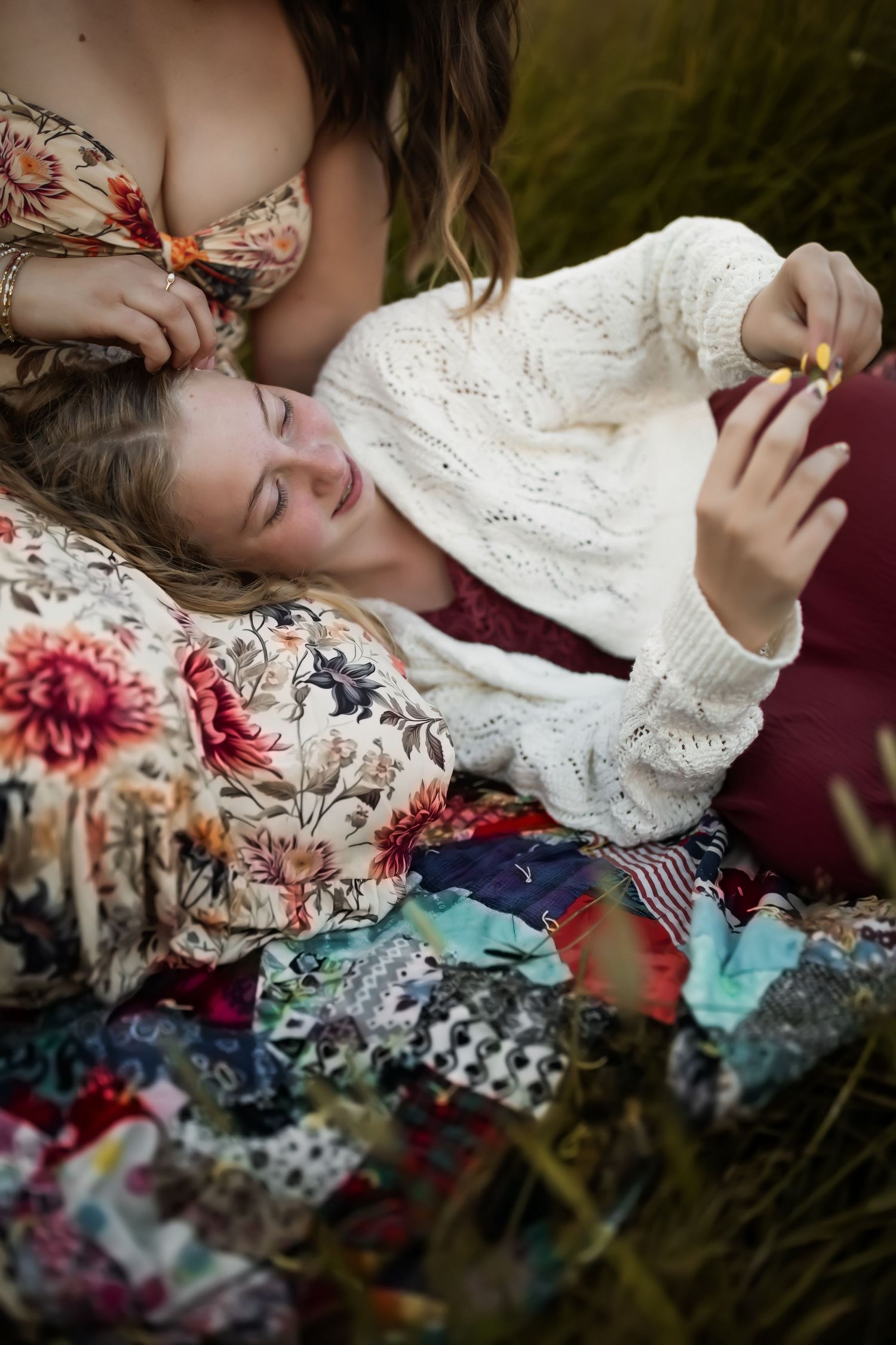 Artistic portrait of person resting on colorful floral quilt in grassy meadow.
